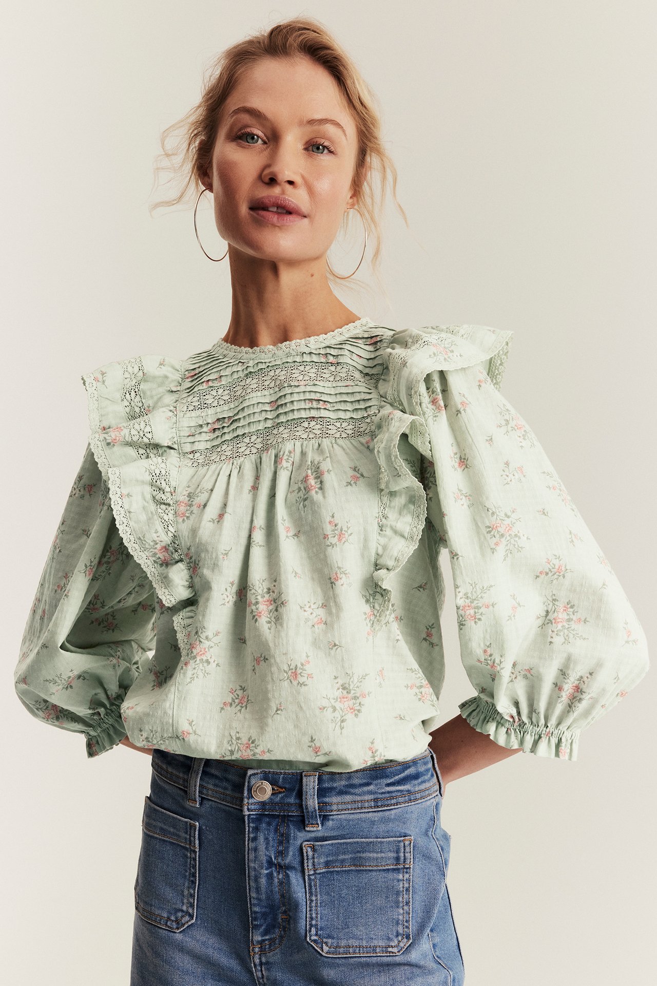 Hellgrüne florale Baumwollbluse mit Spitze, Smock und Puffärmeln, in blaue Jeans gesteckt, getragen von Frau.