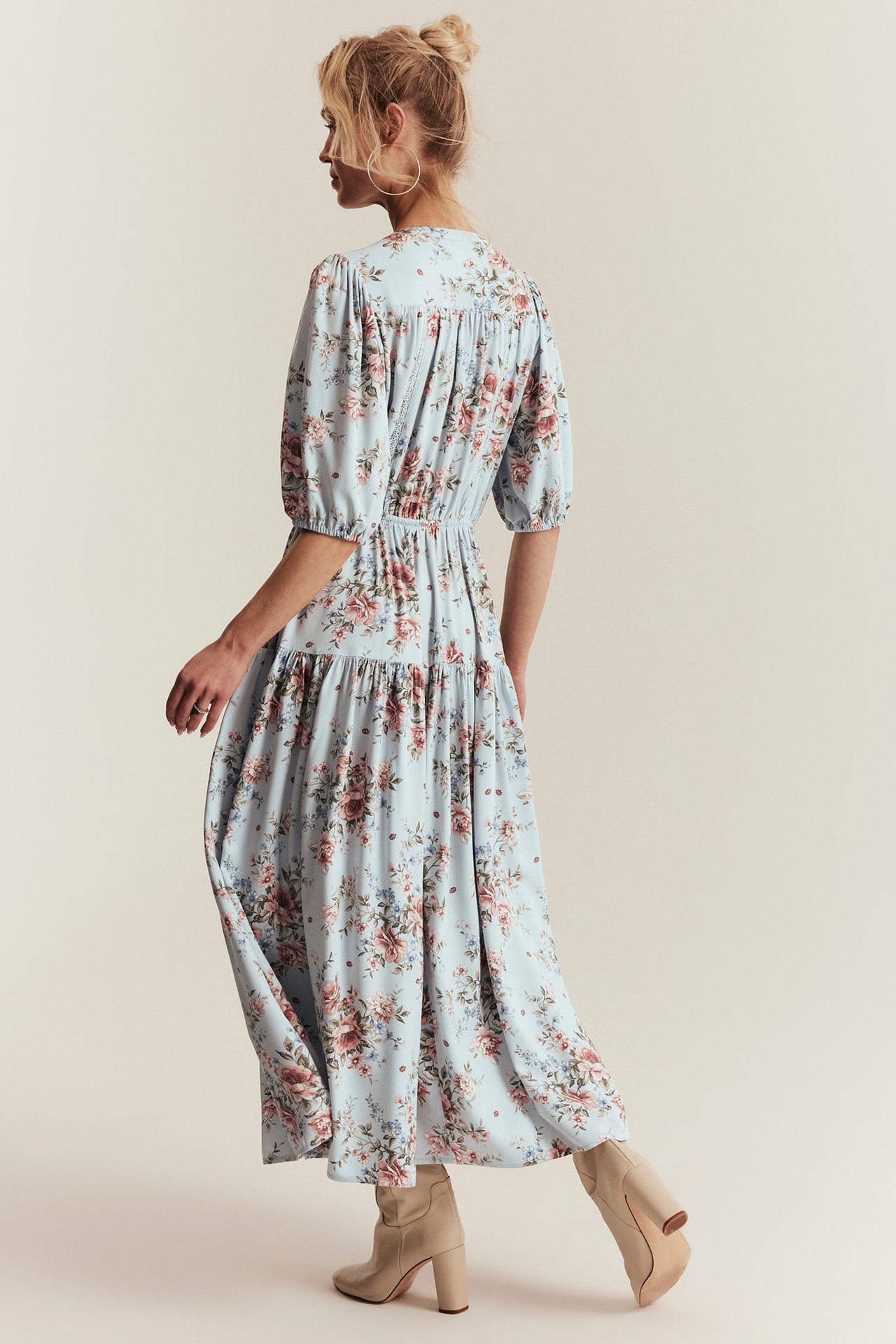 Seitenansicht von hinten einer Frau in hellblauem, geblümtem Viskose-Maxikleid und hellbeigen Stiefeletten.