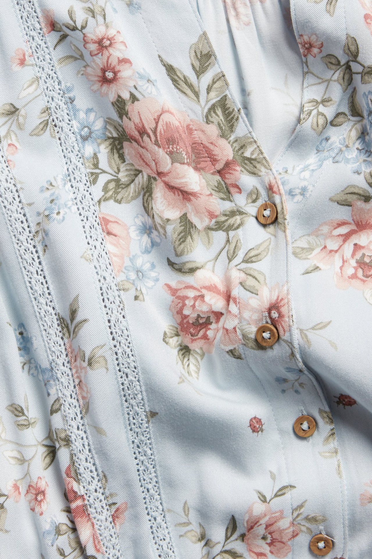 Nahaufnahme eines hellblauen geblümten Viskosekleides mit Spitzenbesatz und kleinen Holzknöpfen.