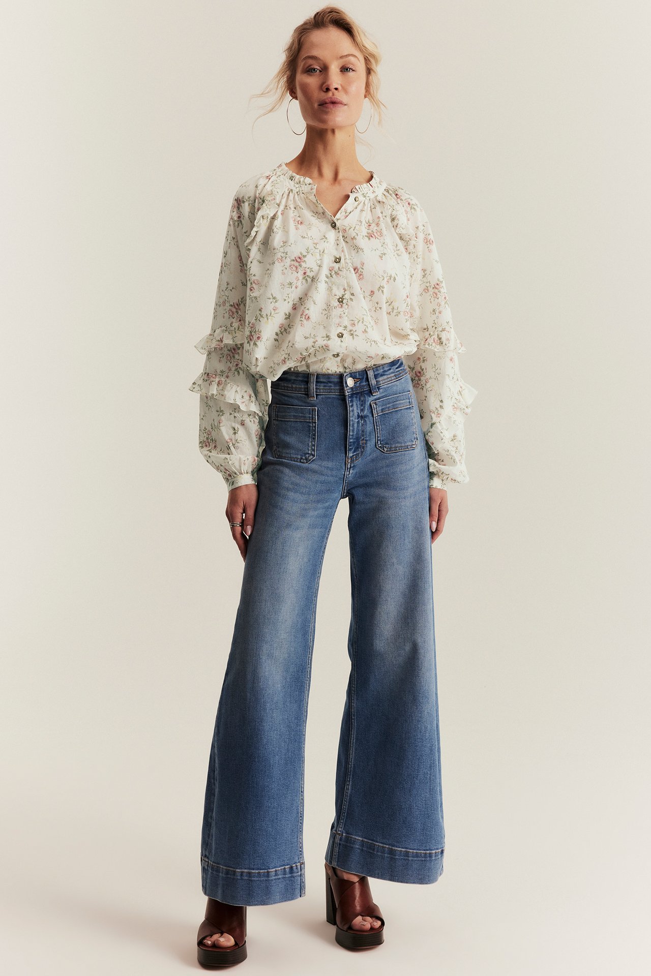 Front view of a woman in an off-white floral blouse, blue wide-leg jeans, and brown platform heels.