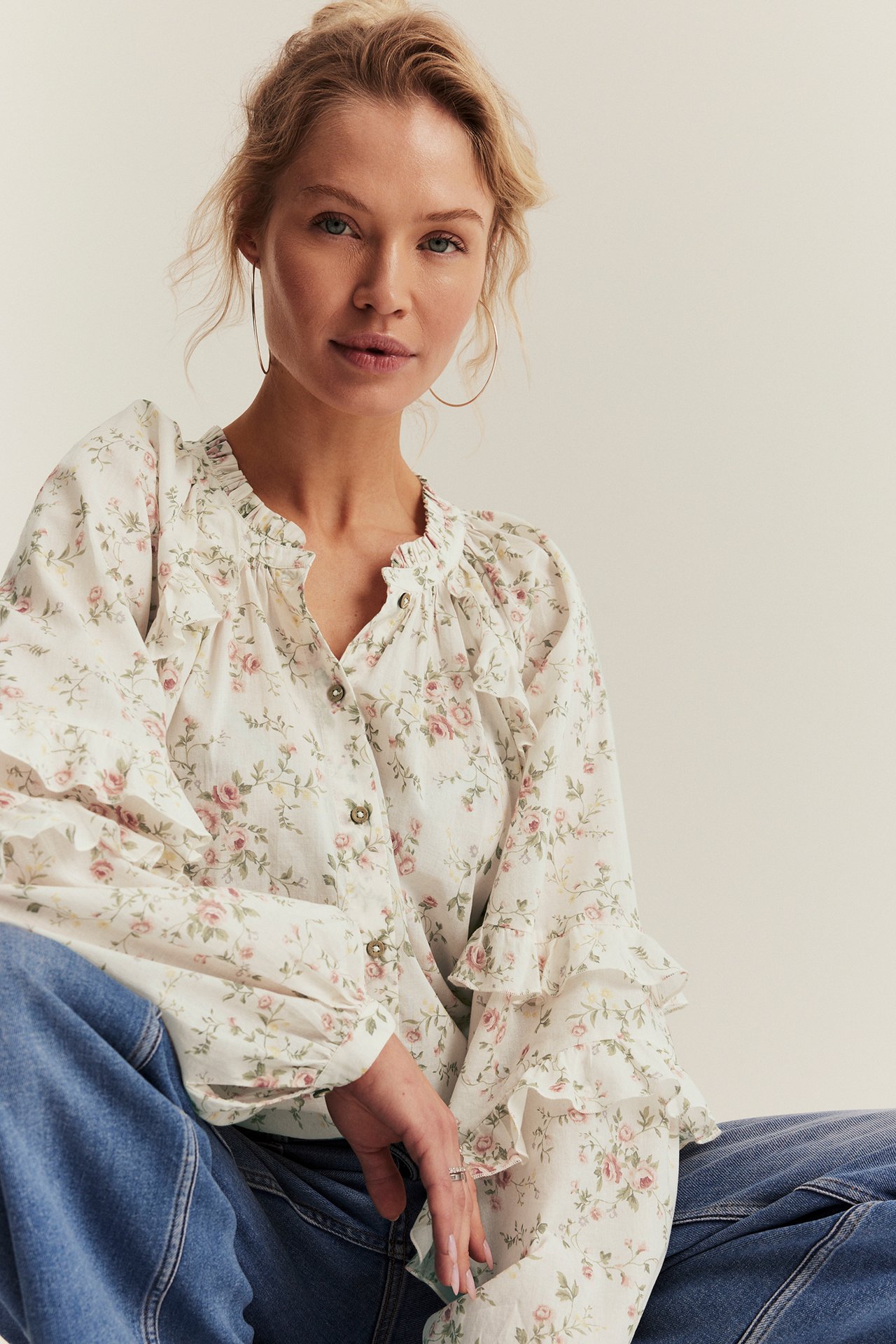 Front view of a woman in an off-white floral cotton ruffled blouse with buttons, blue jeans.