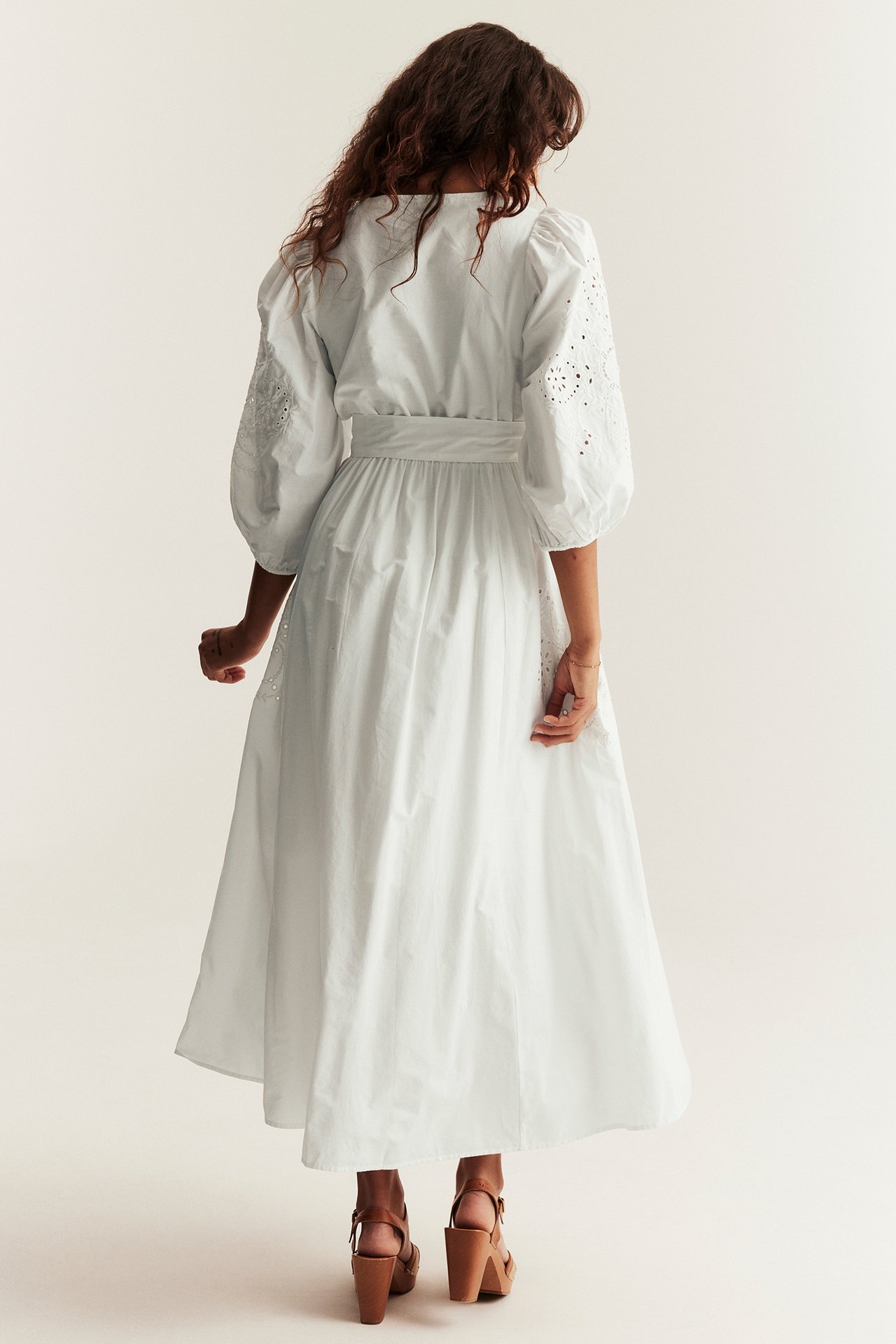 Rückenansicht einer Frau im off-white bestickten Baumwoll-Maxikleid mit Puffärmeln und braunen Keilsandalen.