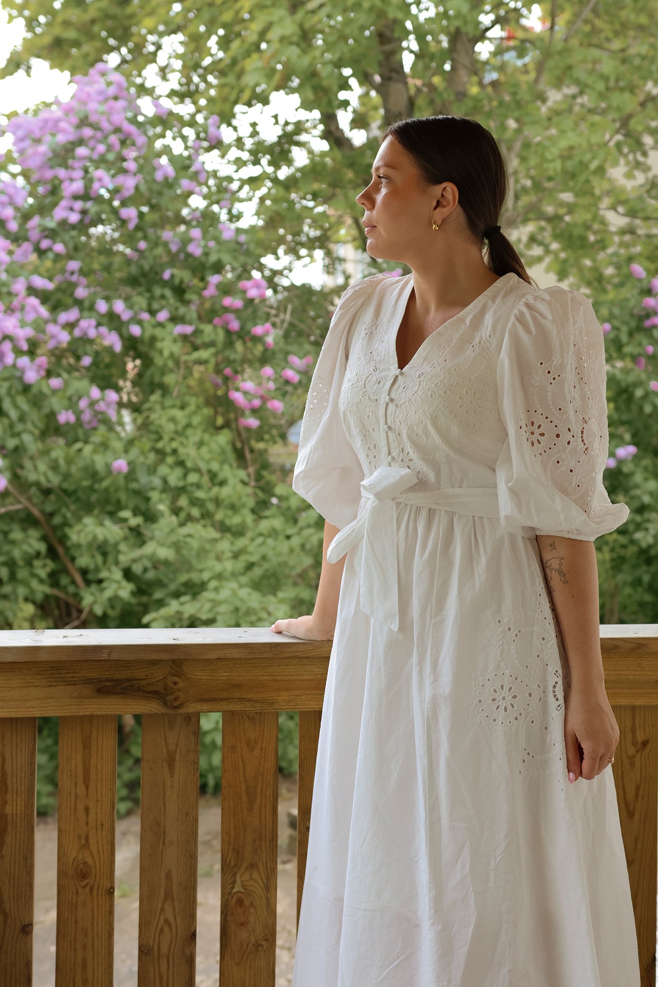 Side view of a woman in an off-white embroidered cotton midi dress with puff sleeves and a tied waist.