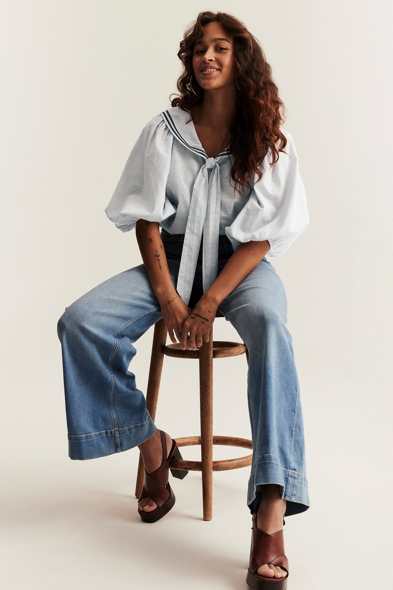 Front view of a woman wearing a blue striped sailor blouse with puff sleeves, wide-leg jeans, and brown platform sandals.