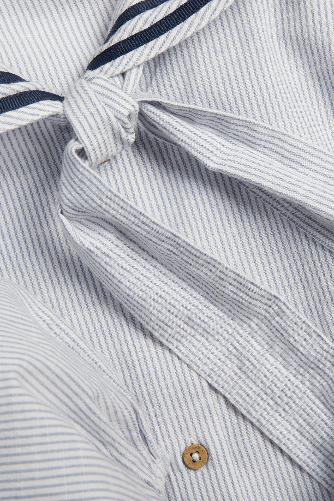 Close-up of a blue and white striped cotton woman's blouse with sailor collar, navy ribbons, front tie-knot, wooden button.