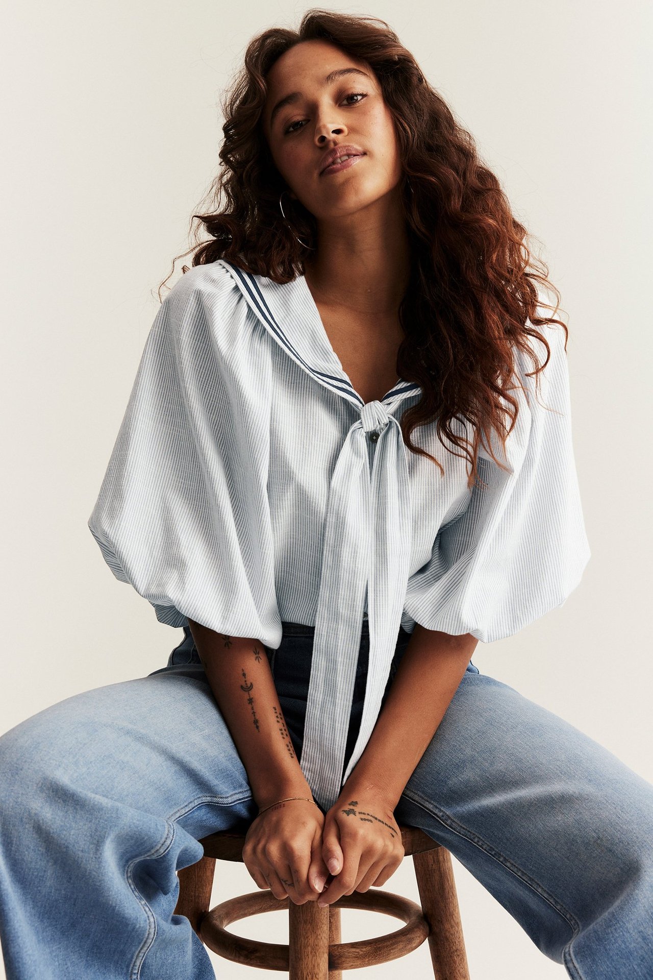 Front view: Woman in striped blue sailor blouse, puffed sleeves, tie-neck, and light blue jeans.