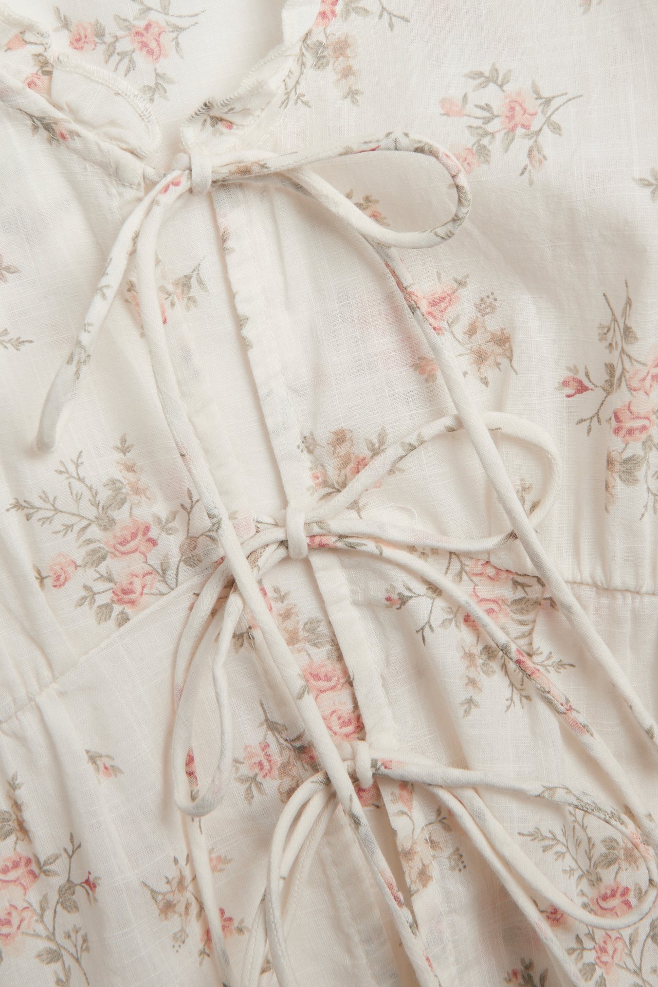 Close-up front view of an off-white cotton blouse with a pink floral pattern and front tie details.