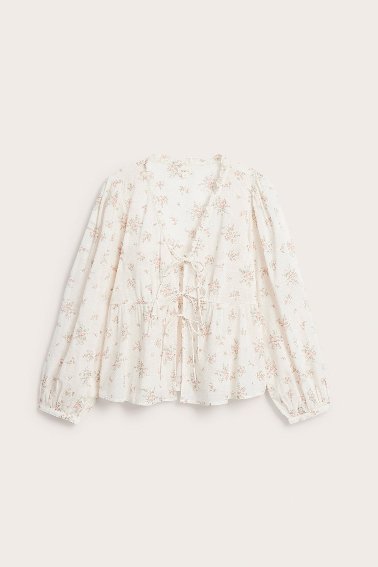 Front view of an off-white cotton floral blouse with a peplum hem and V-neck tie-front.