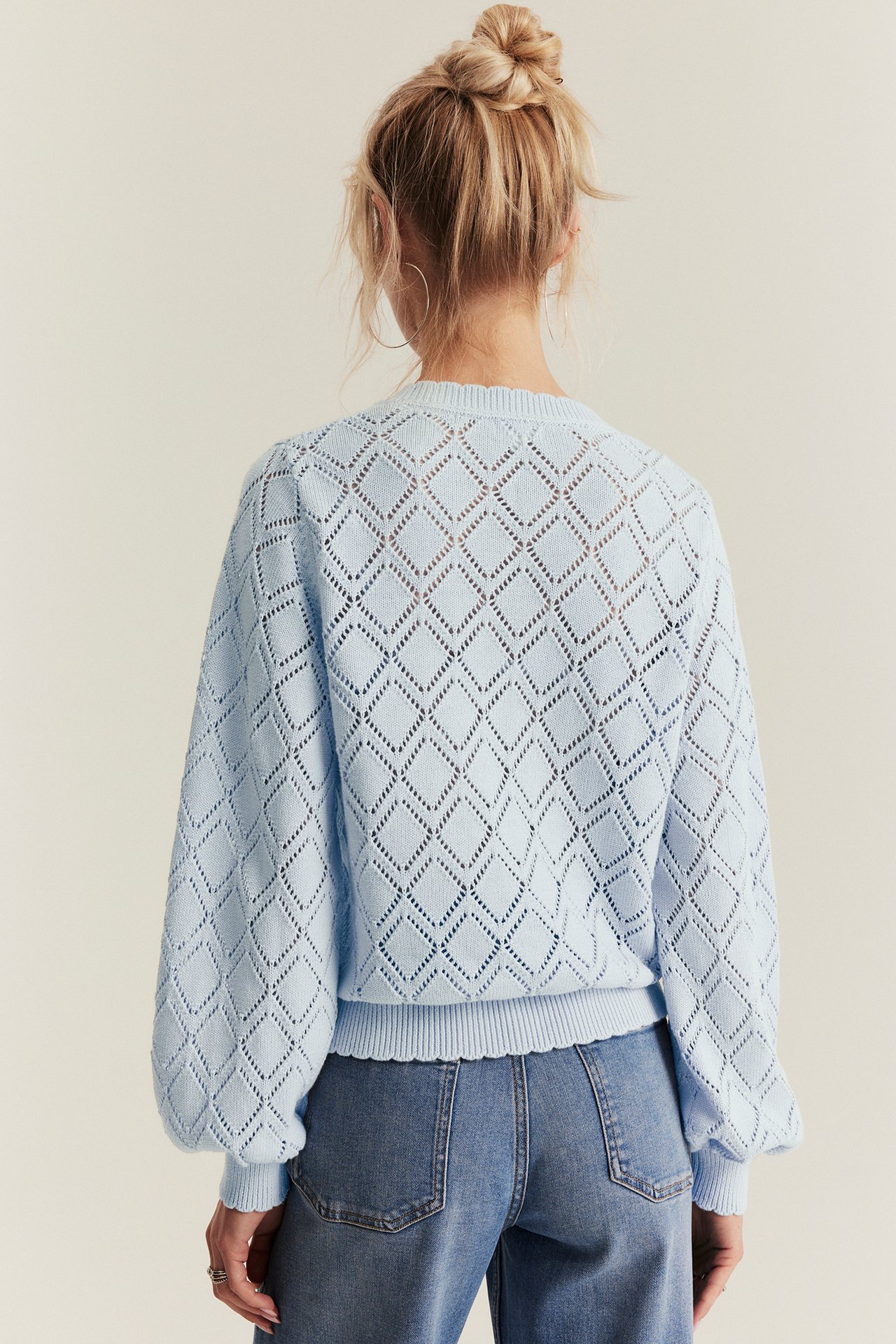 Back view of woman in light blue cotton openwork knit cardigan with long puffed sleeves and blue jeans.