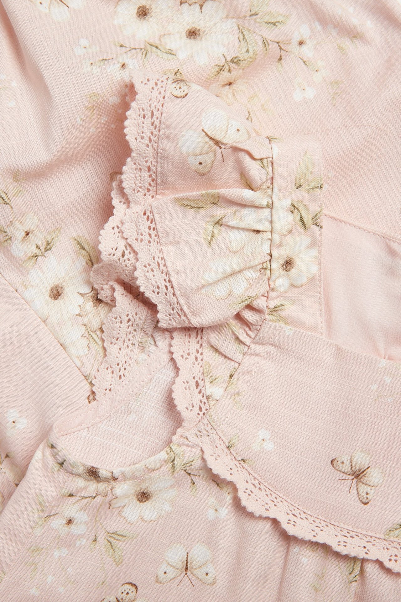 Close-up of a light pink baby cotton coverall with white floral, butterfly print, ruffle sleeves, and lace.