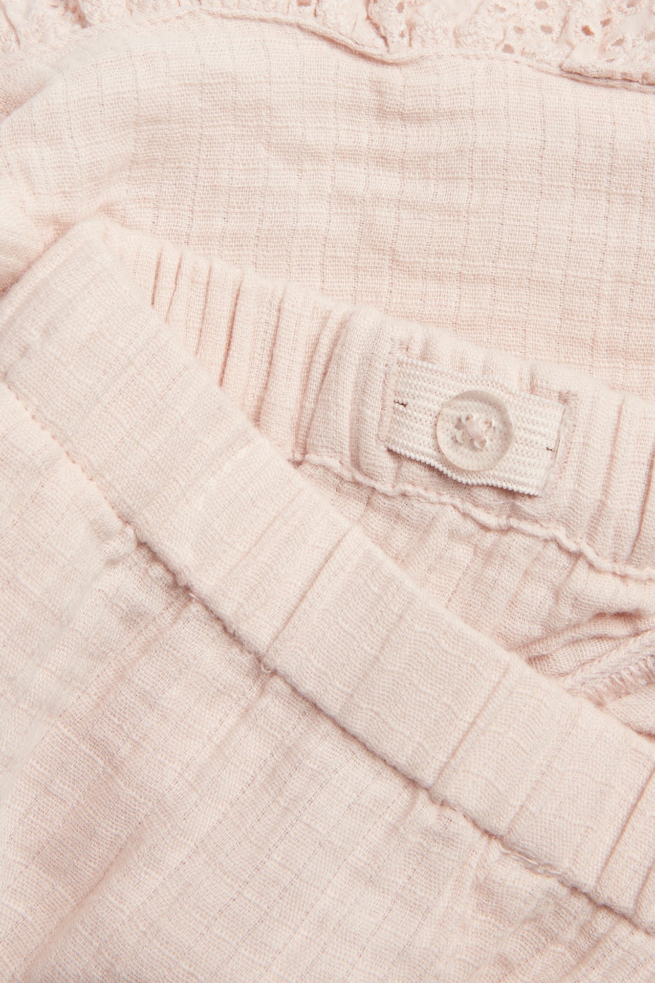 Close-up of light pink woven cotton shorts with an elasticated, adjustable waistband and lace ruffle.