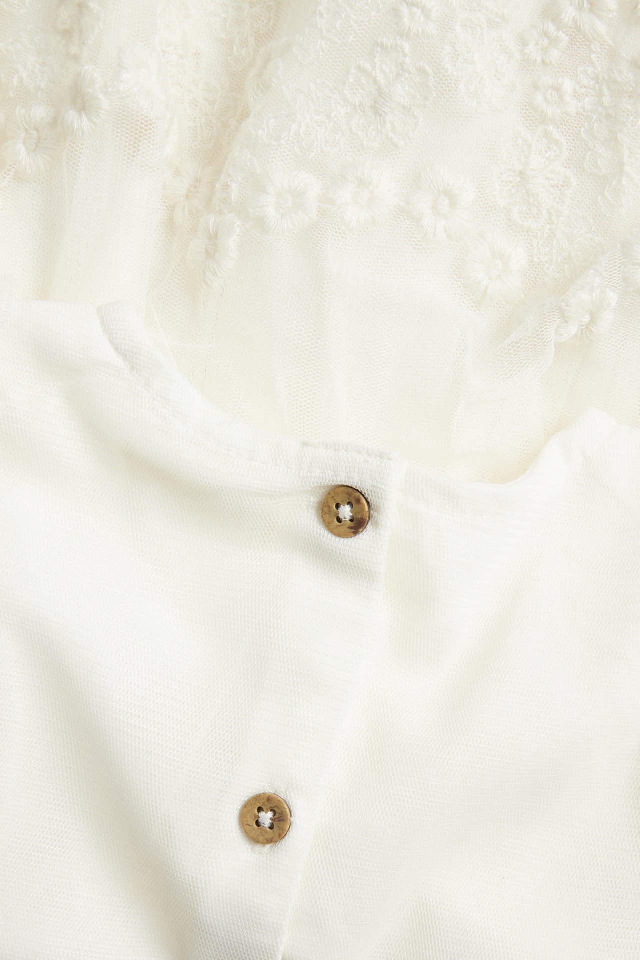 Nahaufnahme der Rückseite eines cremeweißen Mesh-Kleides mit Stickerei und zwei kleinen Holzknöpfen.
