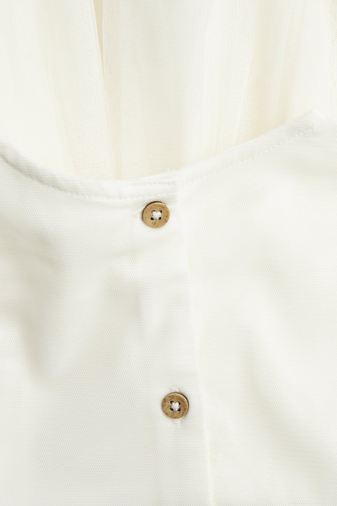 Nahaufnahme eines cremeweißen Meshkleides mit zwei braunen Knöpfen auf Baumwollfutter.