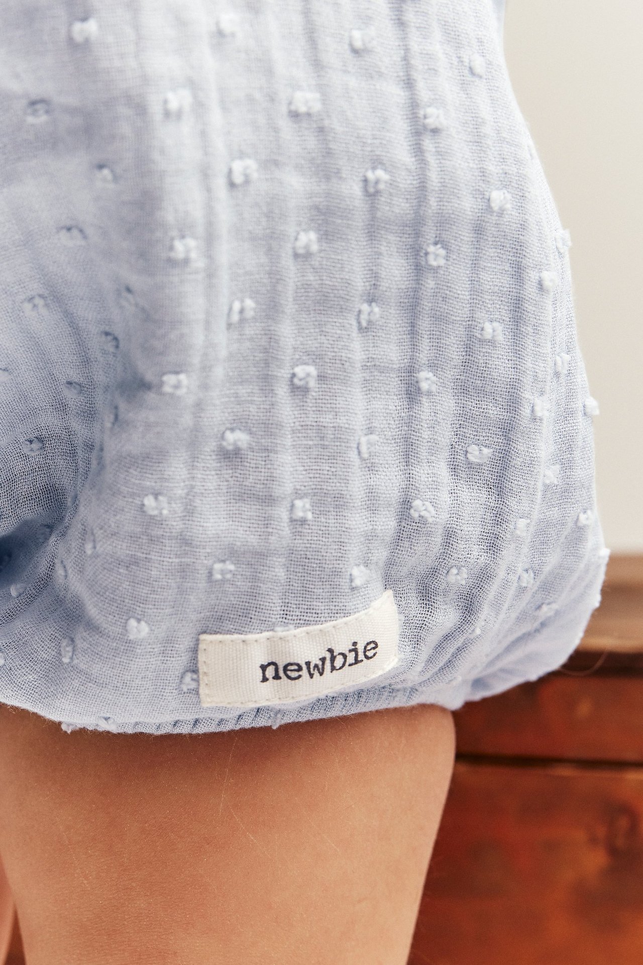 Nahaufnahme vom Babybein in hellblauem strukturiertem Baumwoll-Playsuit mit weißem Stoffetikett.