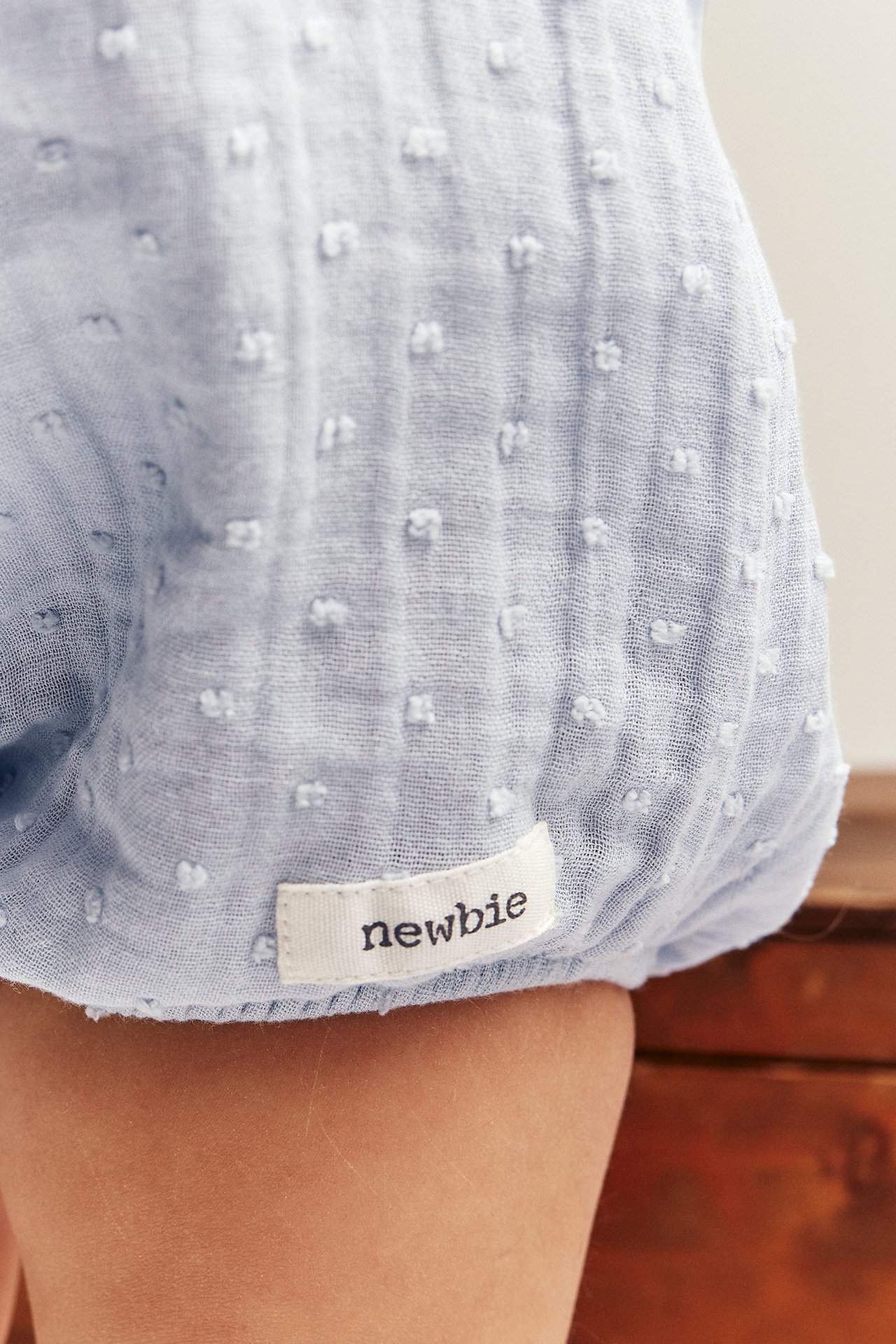 Nahaufnahme vom Babybein in hellblauem strukturiertem Baumwoll-Playsuit mit weißem Stoffetikett.
