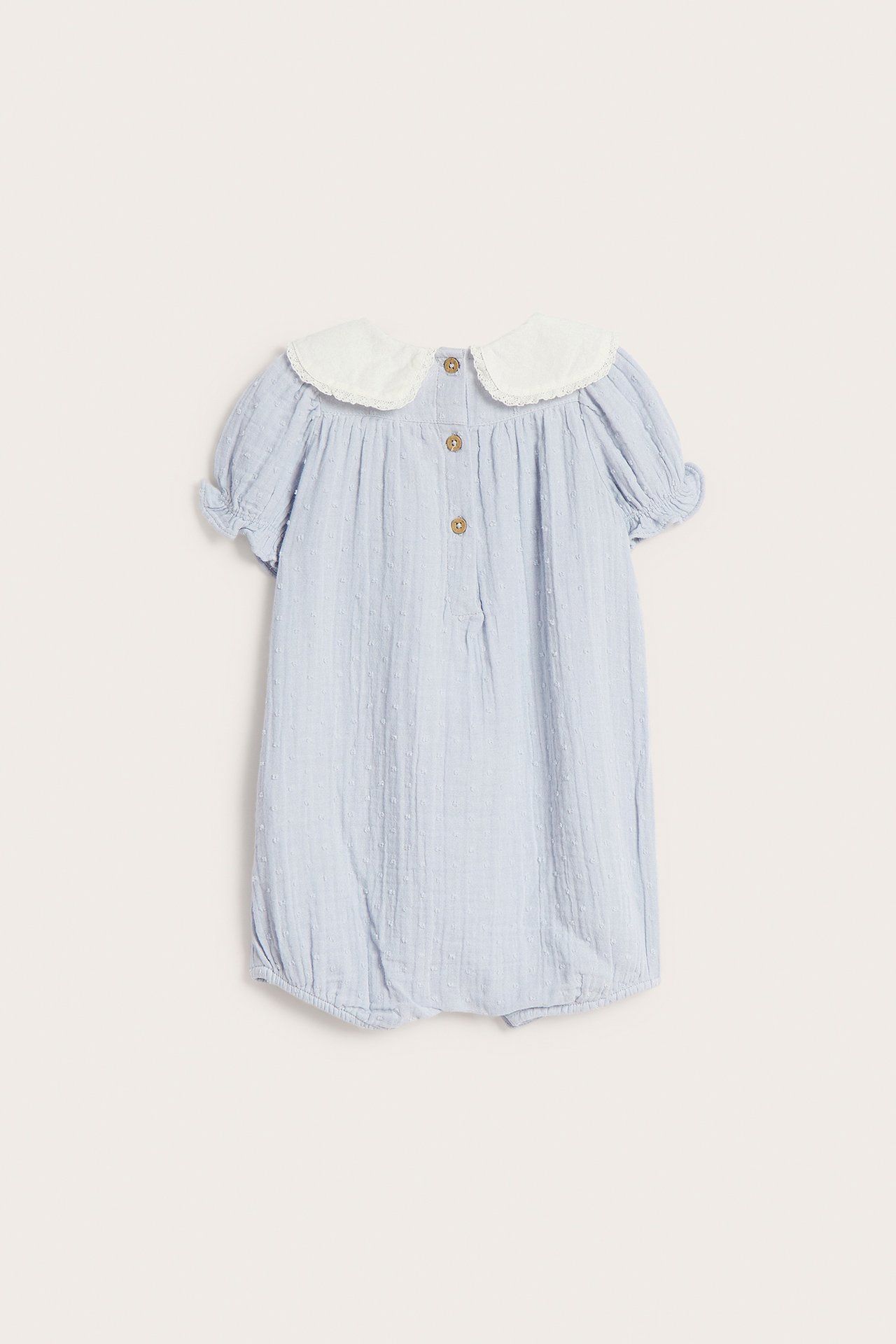 Vorderansicht eines hellblauen Baby-Playsuits mit dezenter Punktstruktur, kurzen Ärmeln, weißem Matrosenkragen und Knöpfen am Rücken.