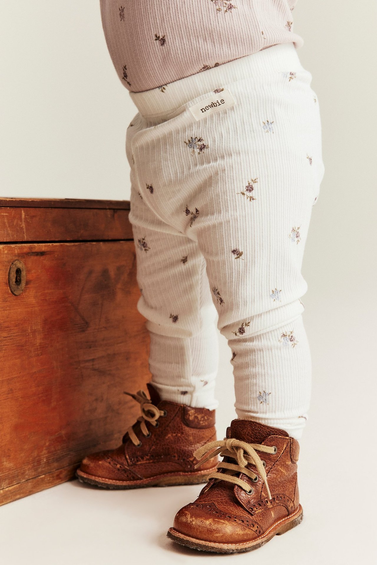 Front view: baby in offwhite ribbed floral leggings, a light purple top, and brown lace-up boots.
