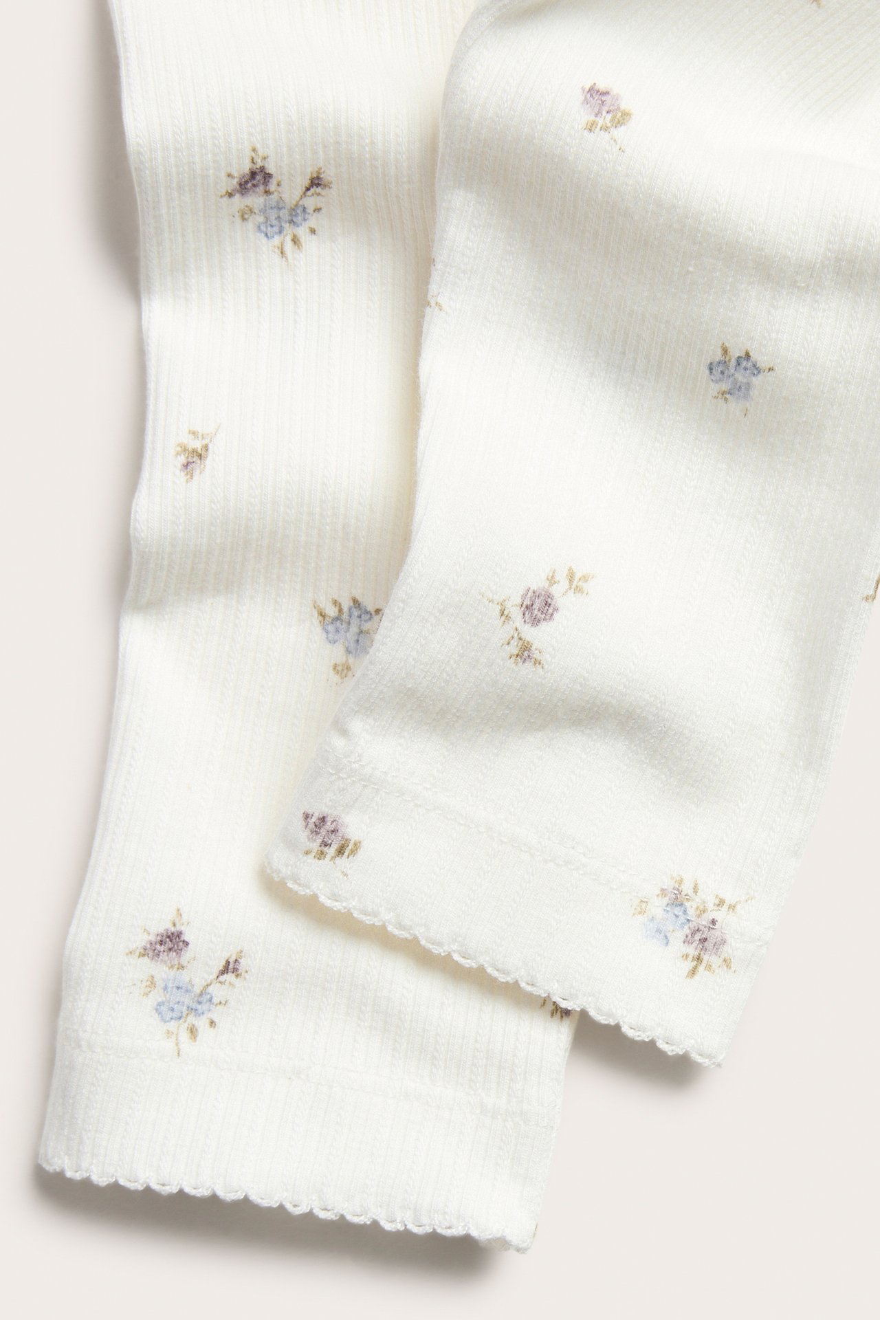 Close-up of off-white ribbed leggings with small floral print and picot trim at the cuffs.
