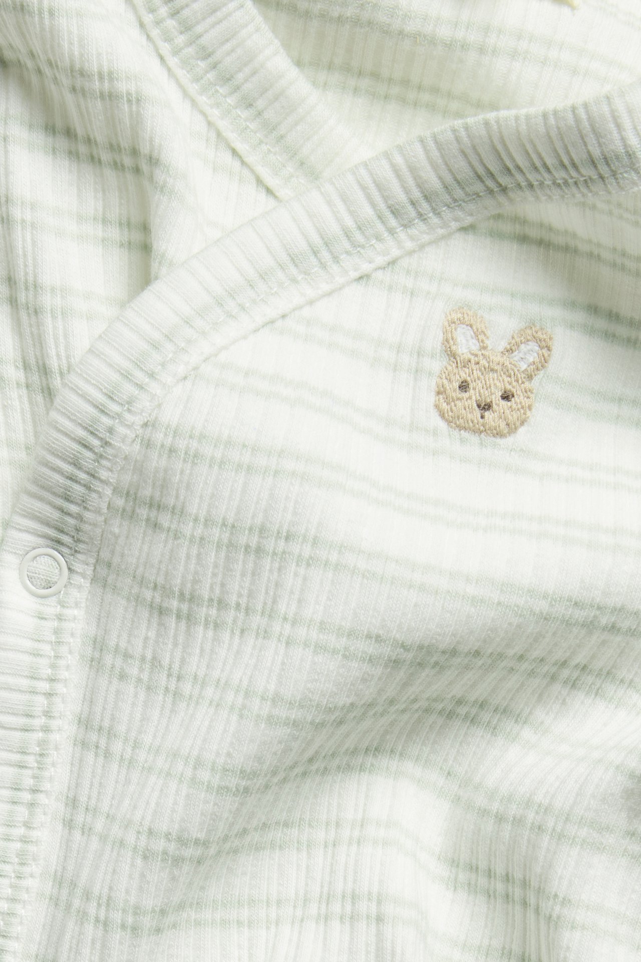Close-up of a striped light green ribbed baby wrap bodysuit with bunny embroidery and a visible snap button.