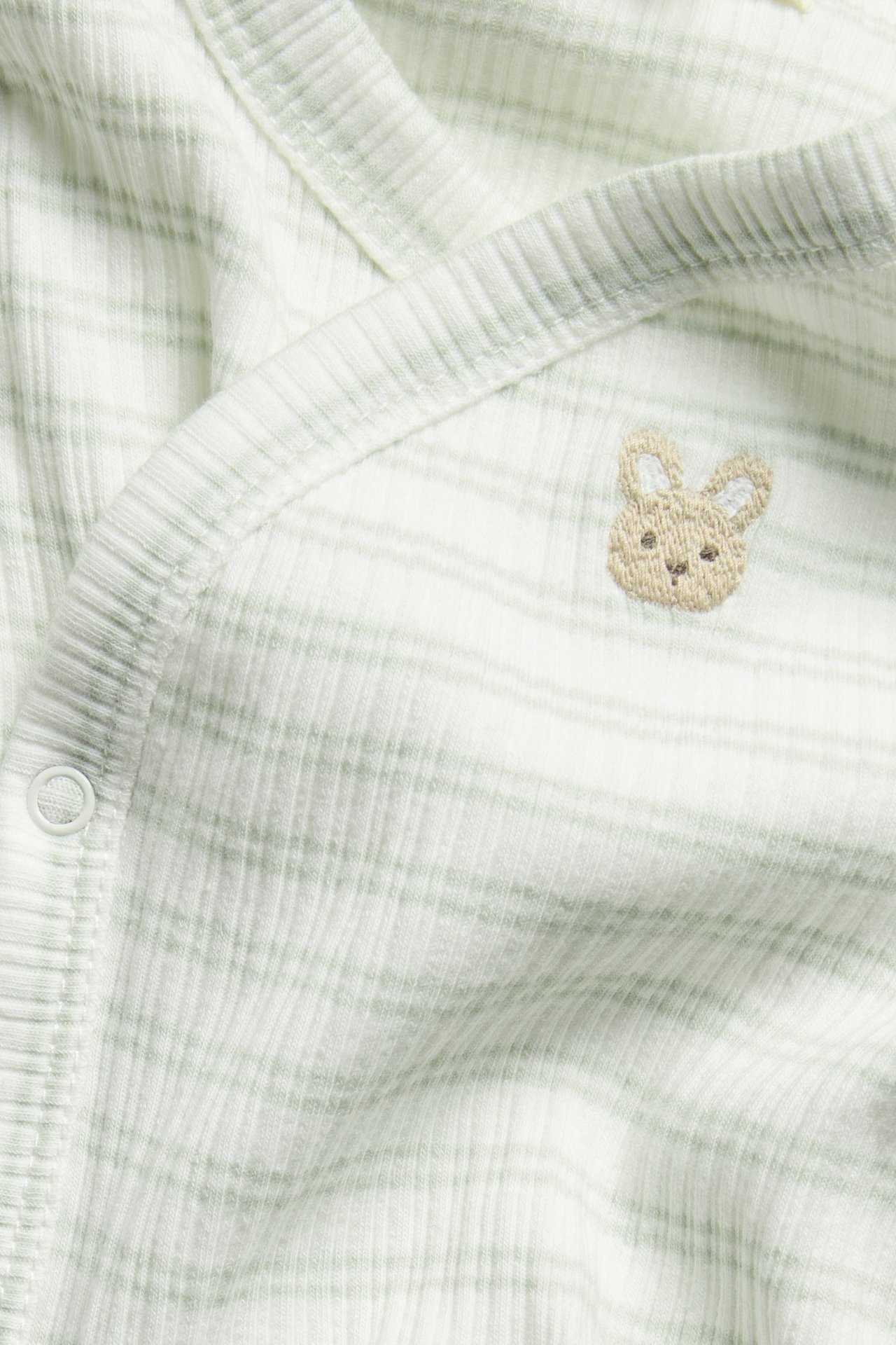 Close-up of a striped light green ribbed baby wrap bodysuit with bunny embroidery and a visible snap button.