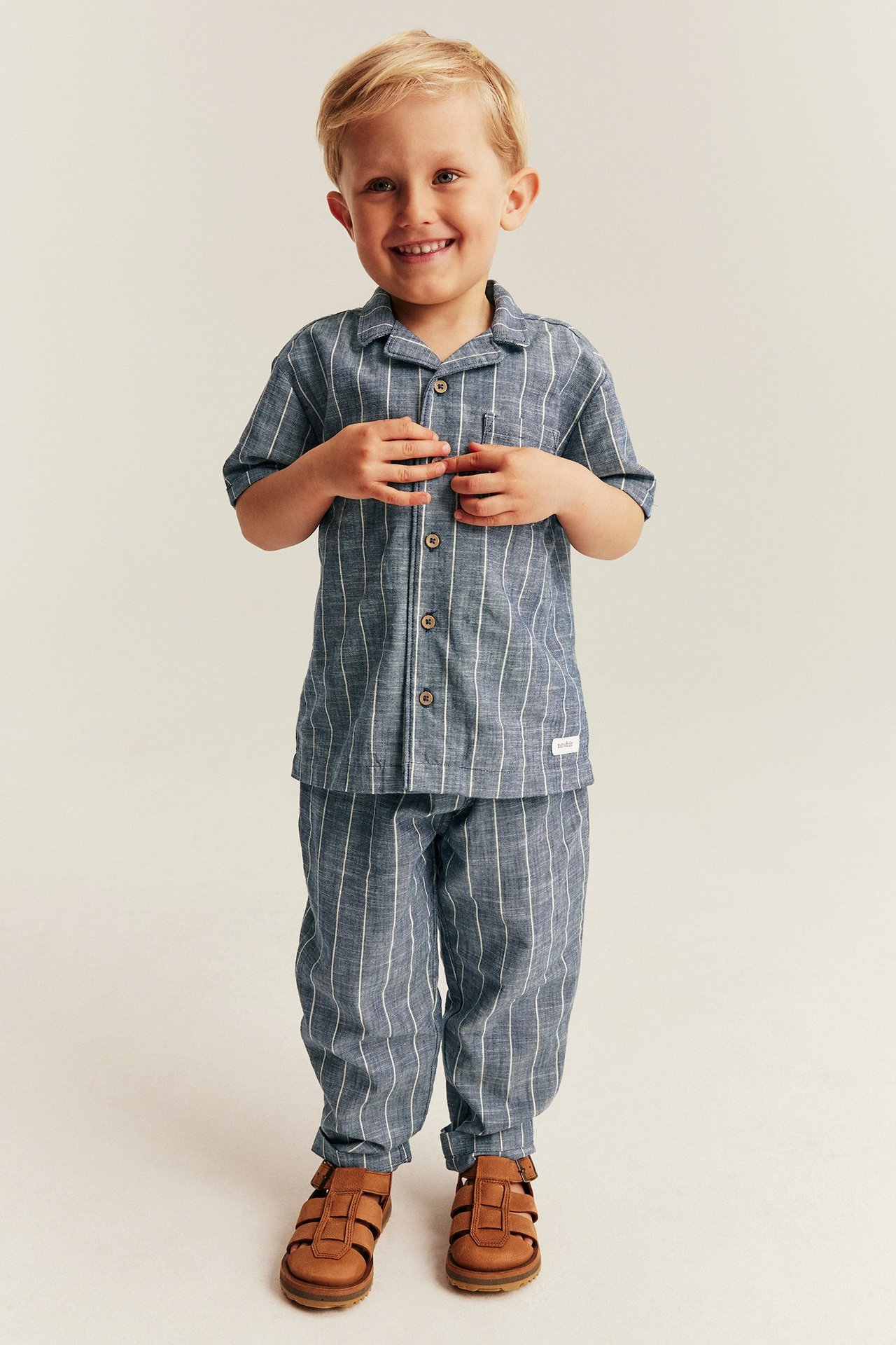 Front view of a kid wearing a blue striped woven short-sleeve shirt, matching pants, and brown sandals.