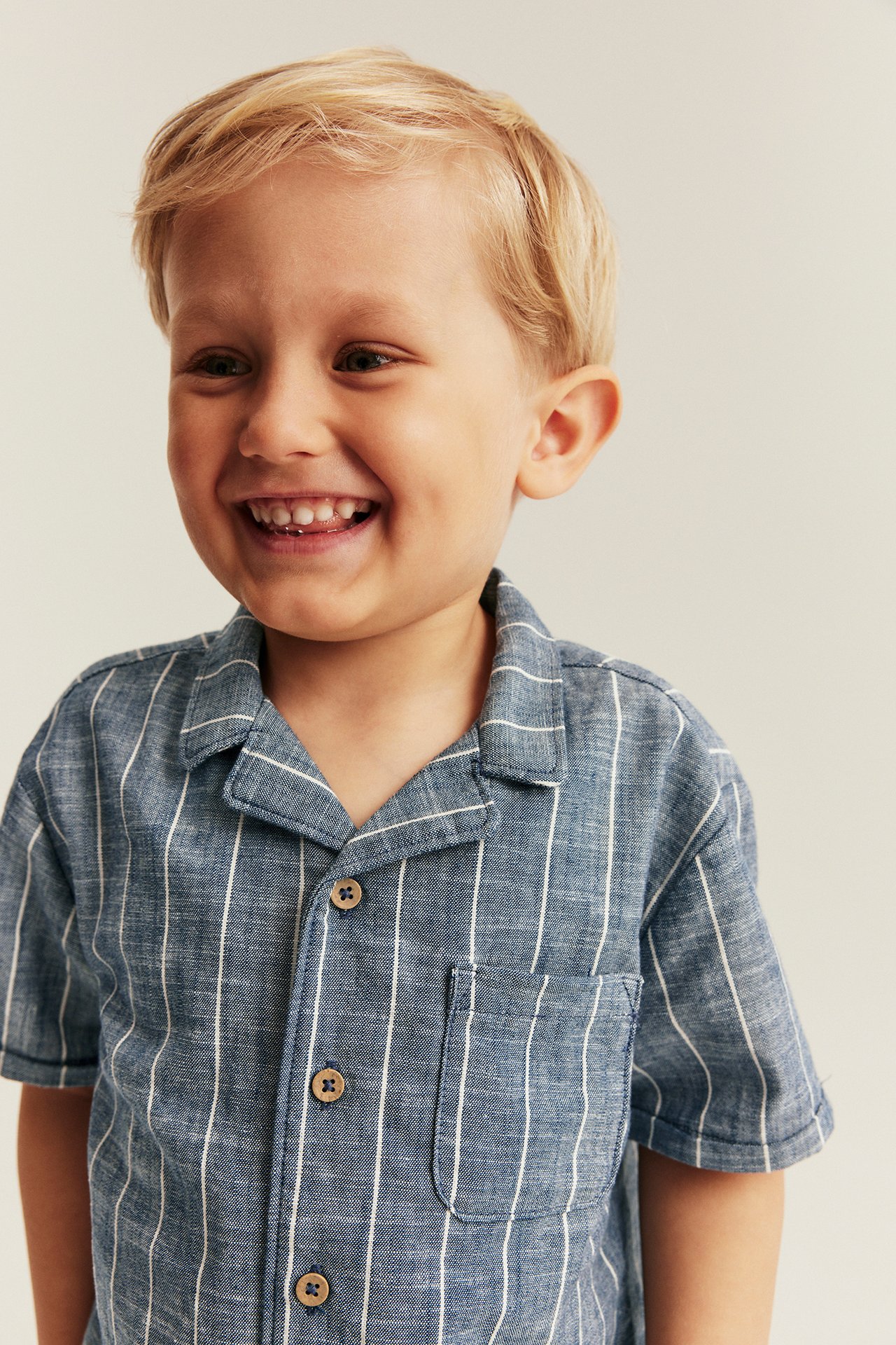 Vorderansicht eines lächelnden Kindes in blau gestreiftem Webhemd mit Kragen und Brusttasche.
