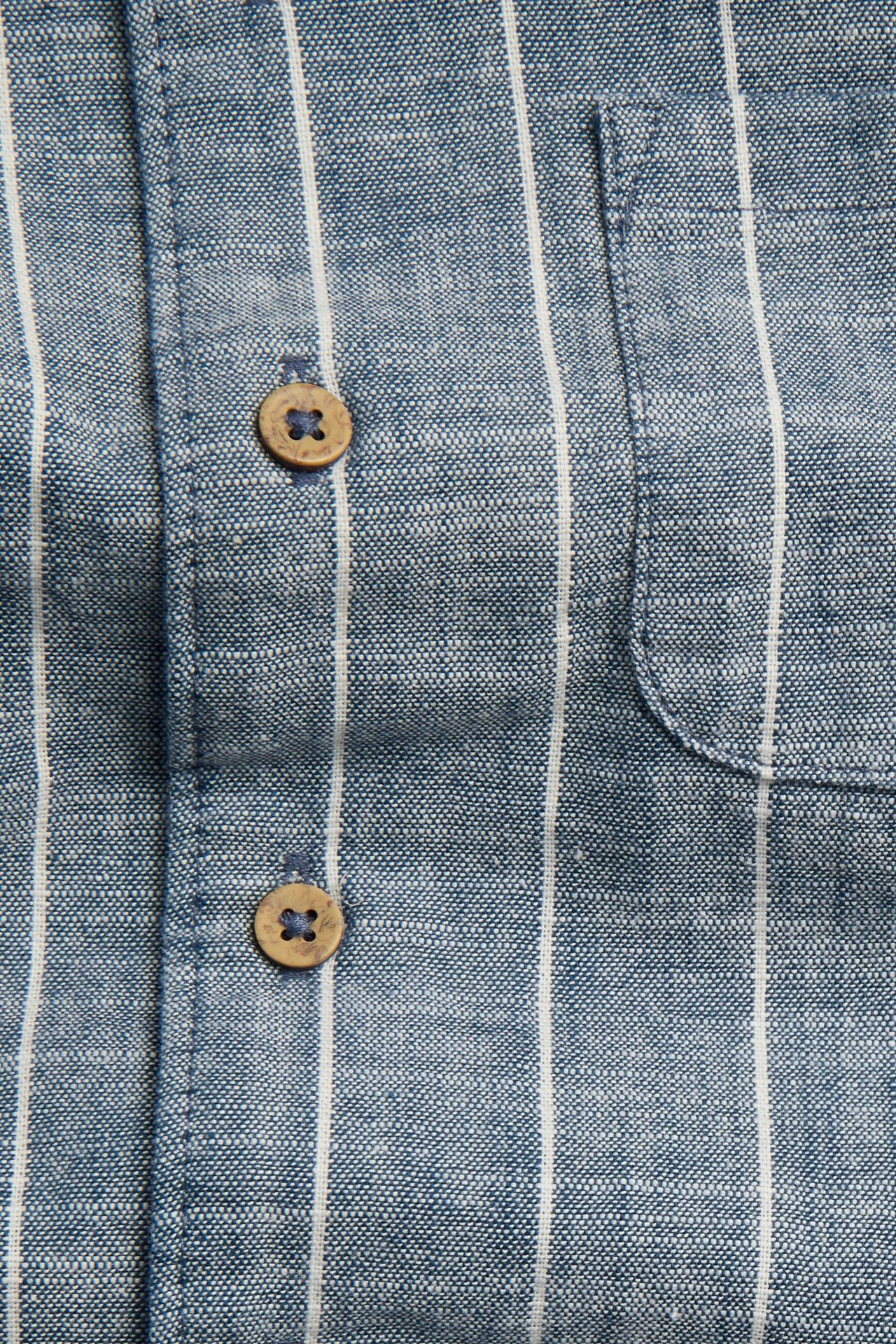 Nahaufnahme eines blau-weiß gestreiften Baumwollwebhemdes mit Brusttasche und Holzknöpfen.