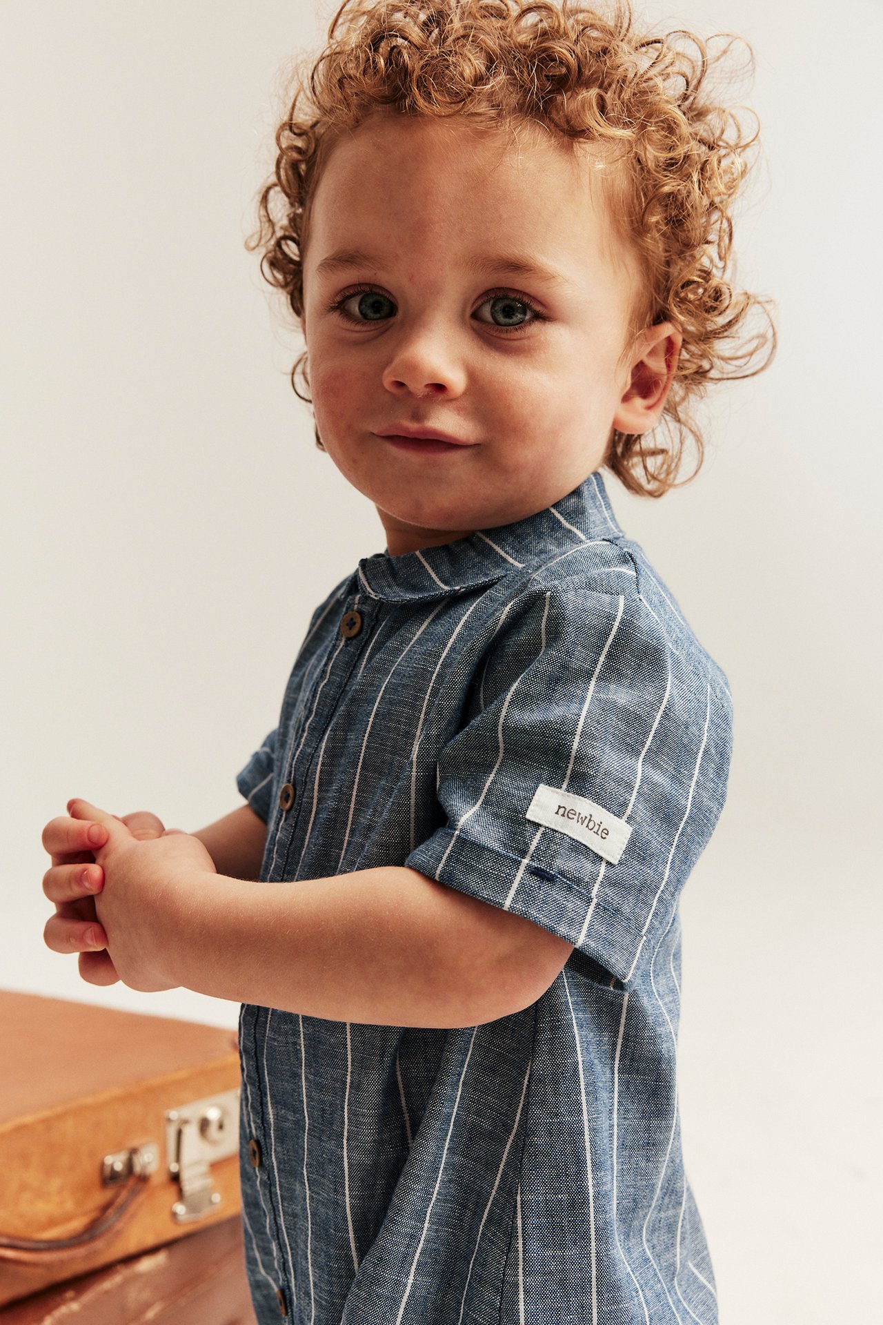 Front view of a baby wearing a blue striped romper with a collar and front buttons.