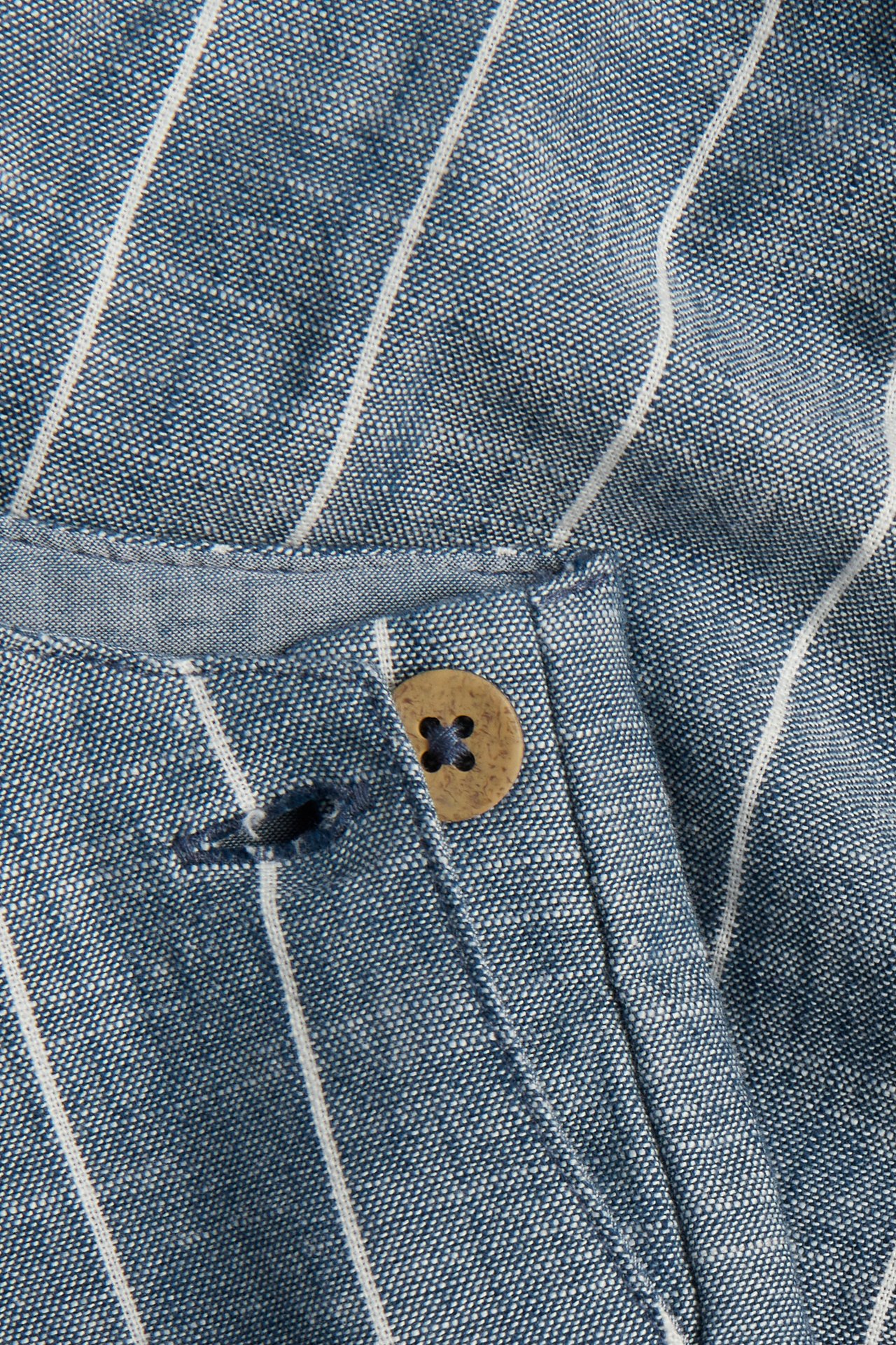 Nahaufnahme einer blau-weiß gestreiften Latzhose aus Baumwolle mit braunem Knopfverschluss.