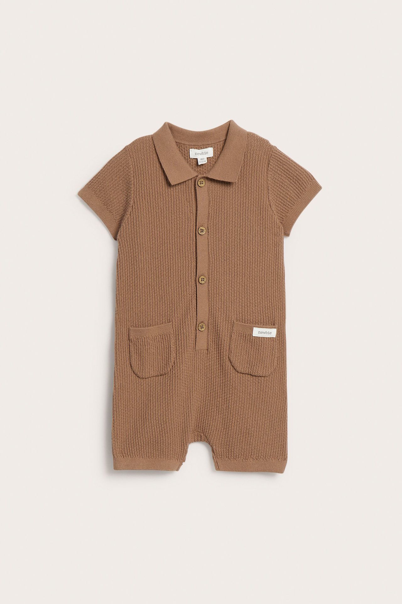 Vorderansicht eines braunen feingestrickten kurzärmeligen Baby-Stramplers mit Kragen, Knöpfen und zwei Taschen.