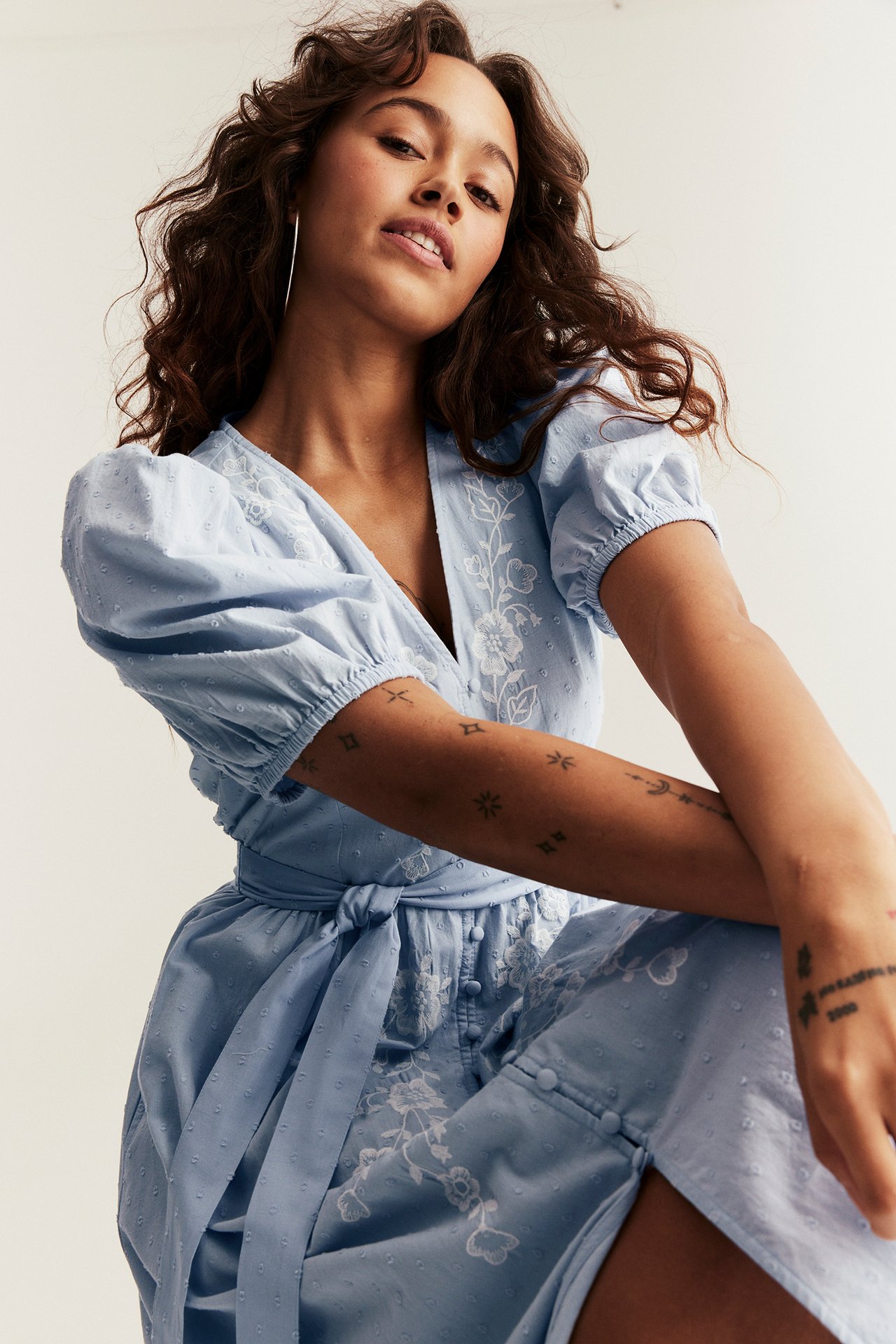 Front view of a woman in a light blue cotton dress with embroidered flowers, puff sleeves, and a tied waist.