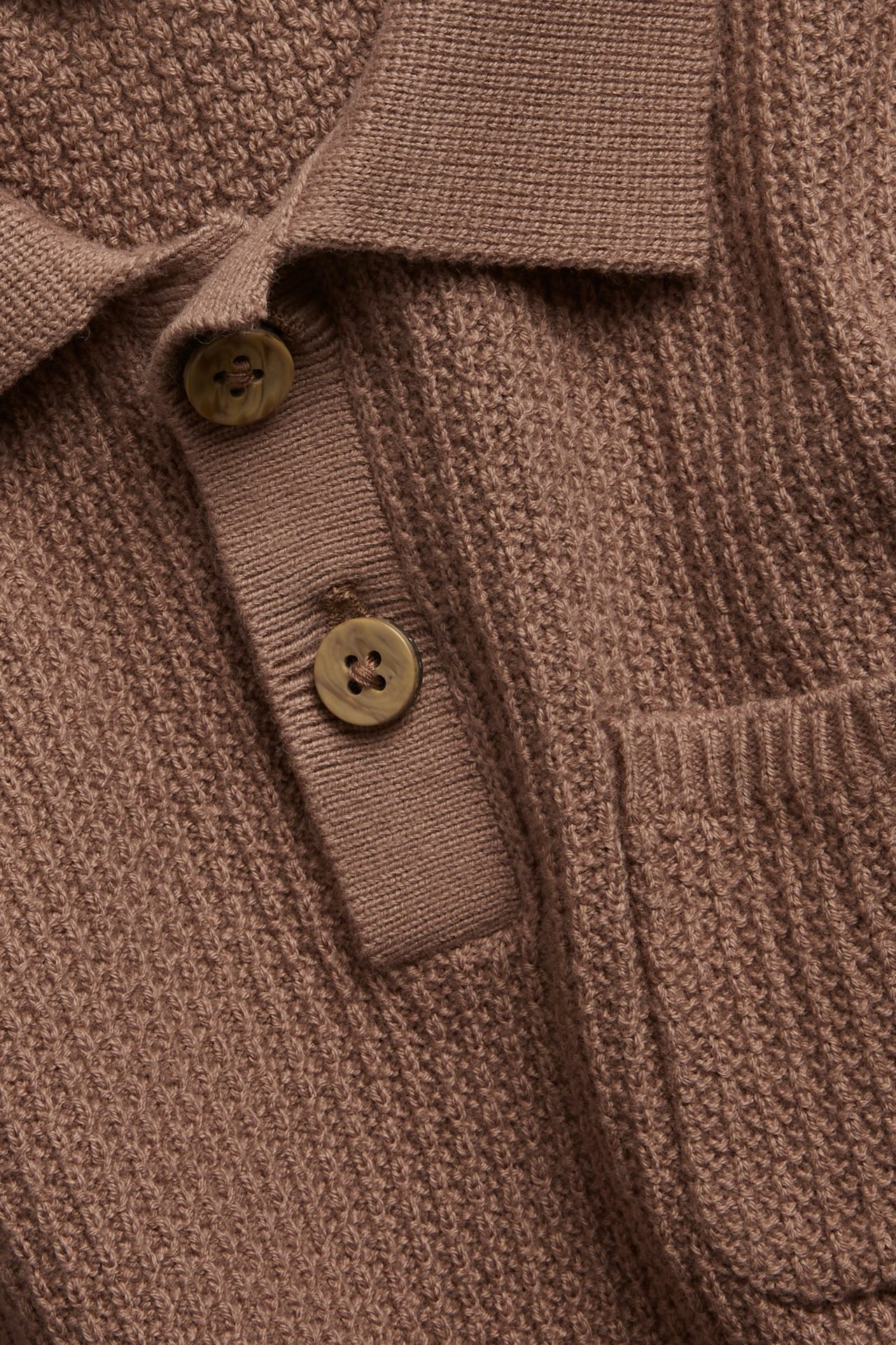 Nahaufnahme von vorn einer braunen gestrickten kurzärmeligen Poloshirts mit Kragen, Knopfleiste und Brusttasche.