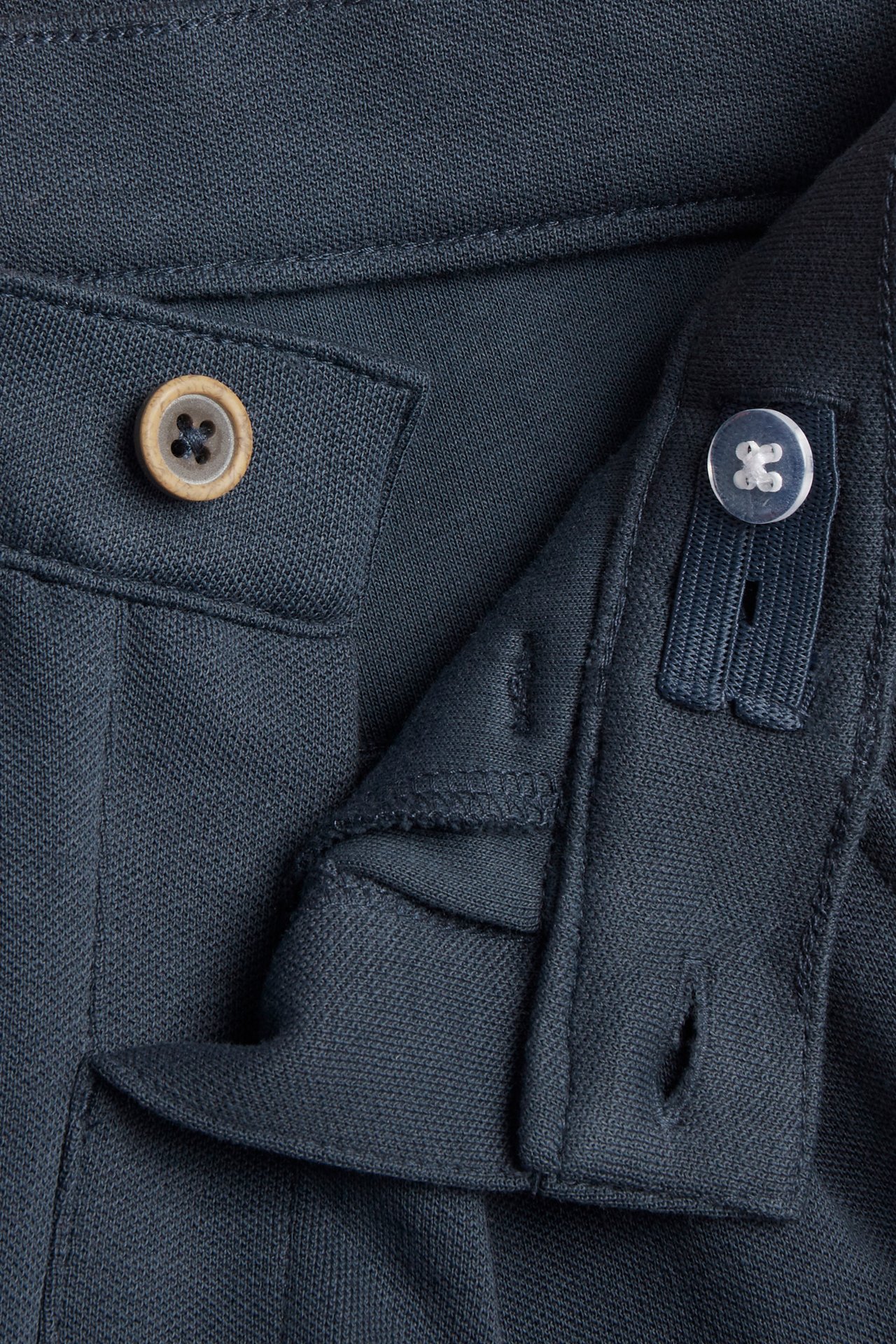 Nahaufnahme von dunkelblauen Kinderhosen mit Knopf vorne und innenliegendem verstellbarem Gummibund.
