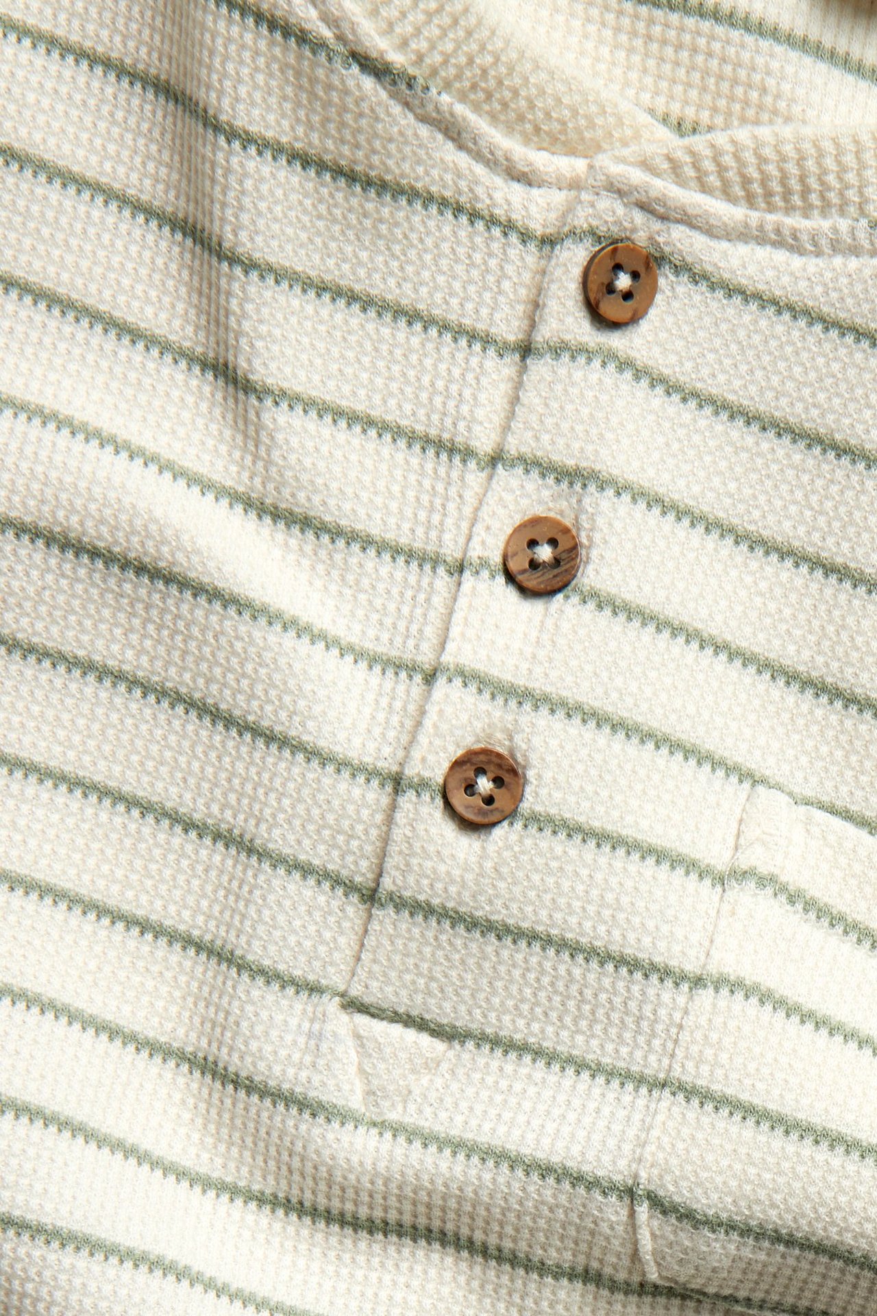 Close-up of a green and white striped waffle top with three wooden buttons and a chest pocket.
