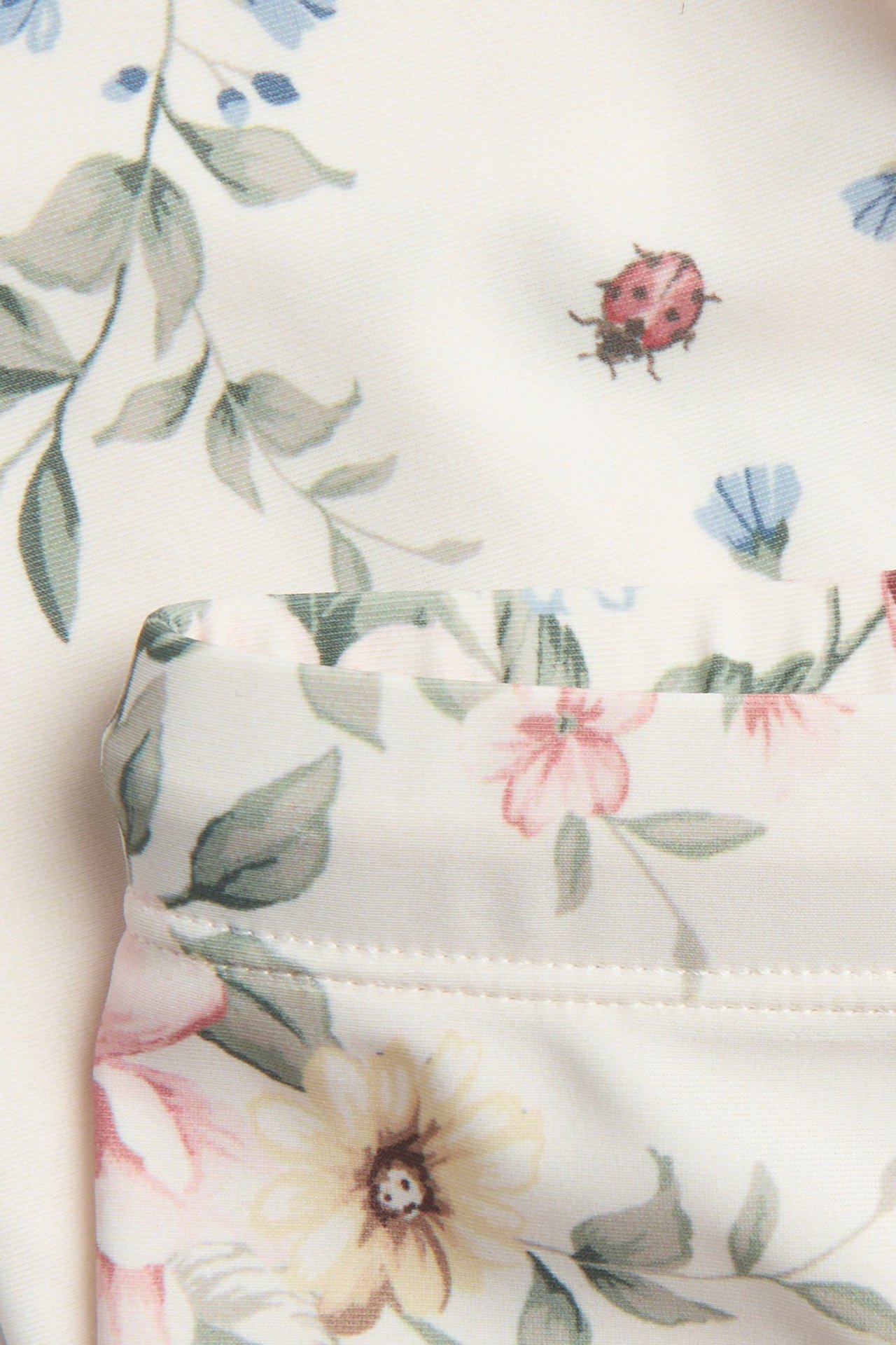 Nahaufnahme von cremefarbenen geblümten dreiviertel UV-Badehosen mit Marienkäferdruck.