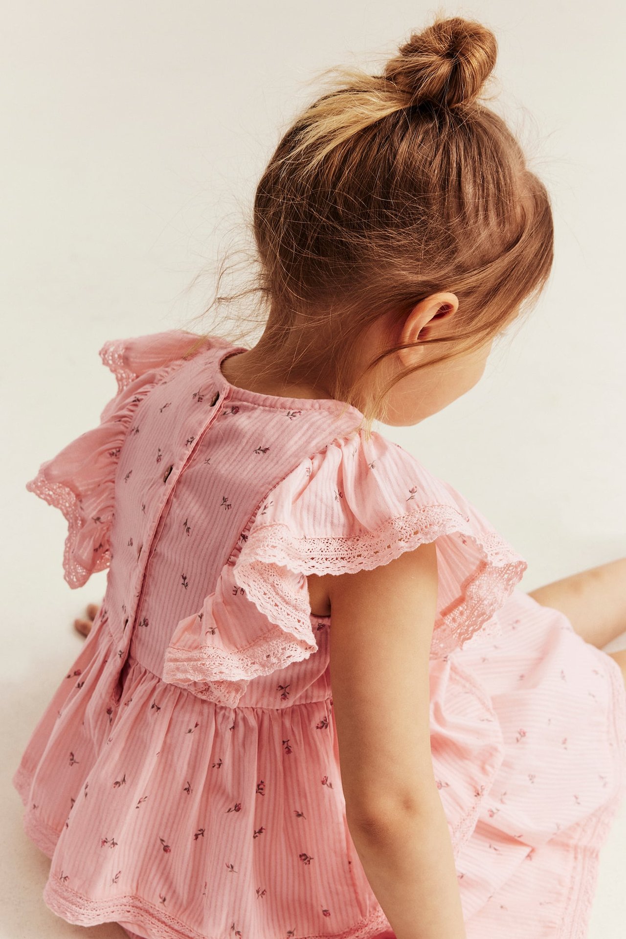 Rückenansicht eines Kindes in hellrosa Blumenkleid mit Streifen, Rüschenärmeln und Knöpfen am Rücken.
