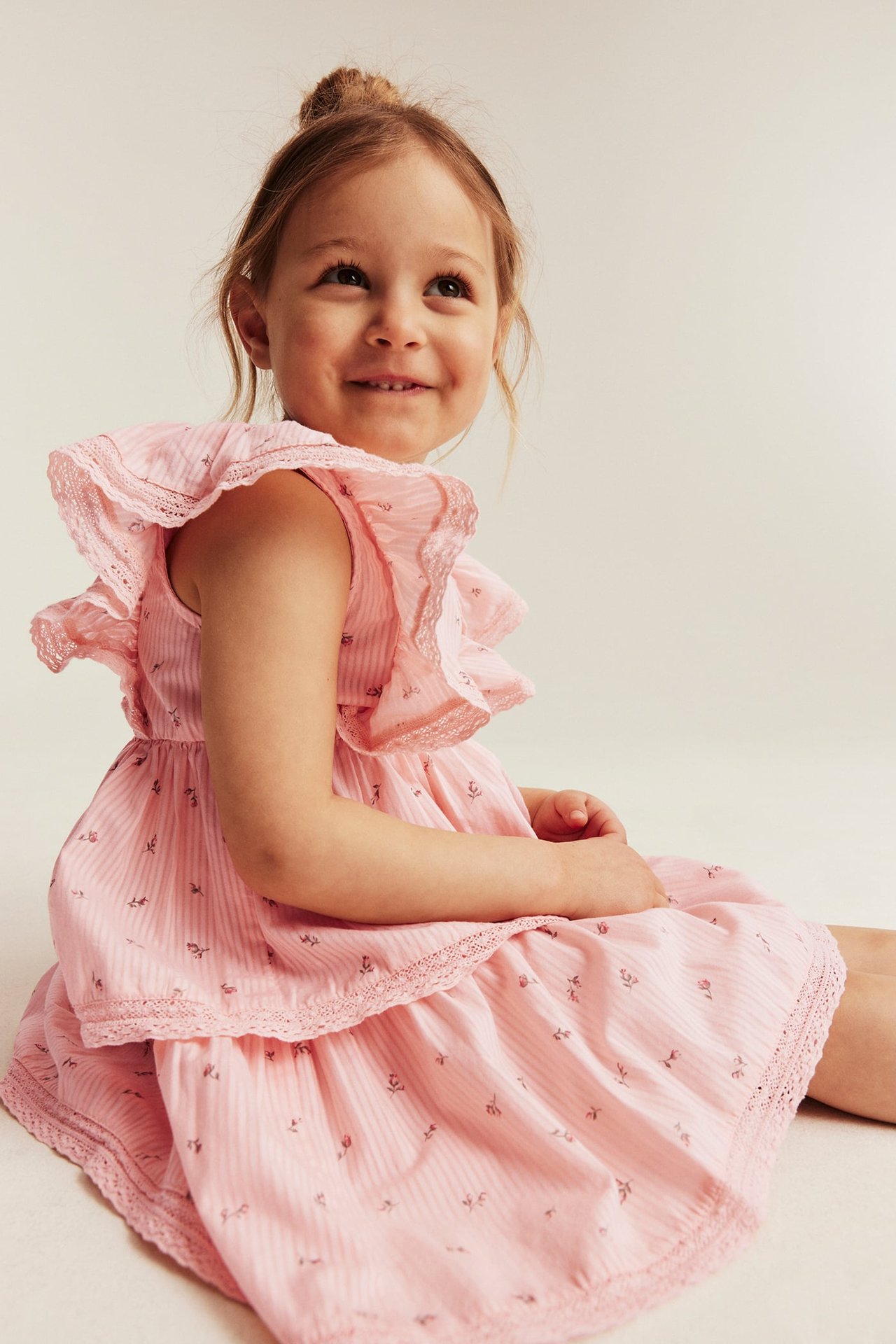 Seitenansicht eines Kindes in hellrosa Blumenkleid mit Streifenstruktur, Rüschenärmeln und Spitzendetails.