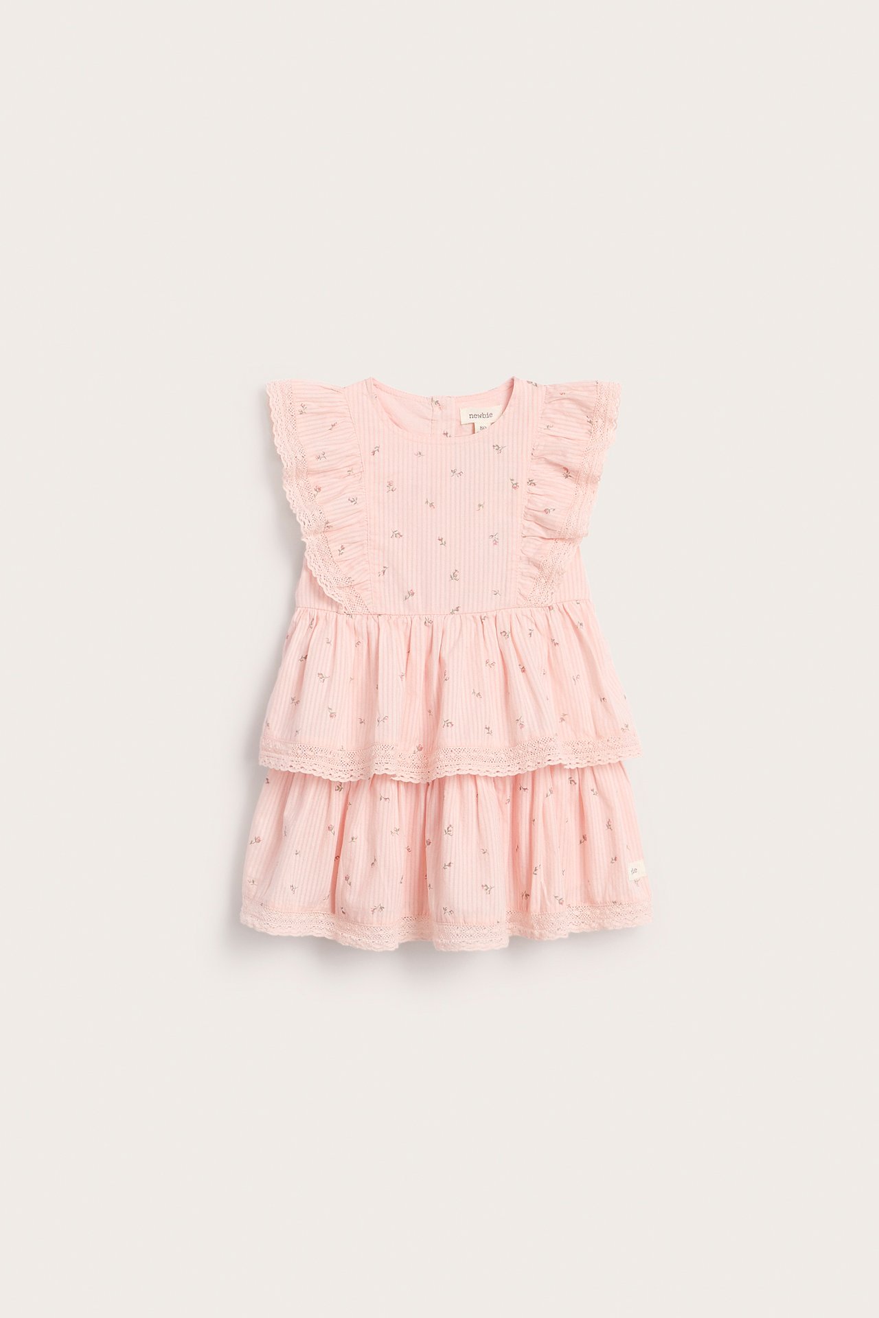 Vorderansicht eines hellrosa gewebten Kinderkleides mit Blumenmuster, Rüschenärmeln und Spitzenkanten.