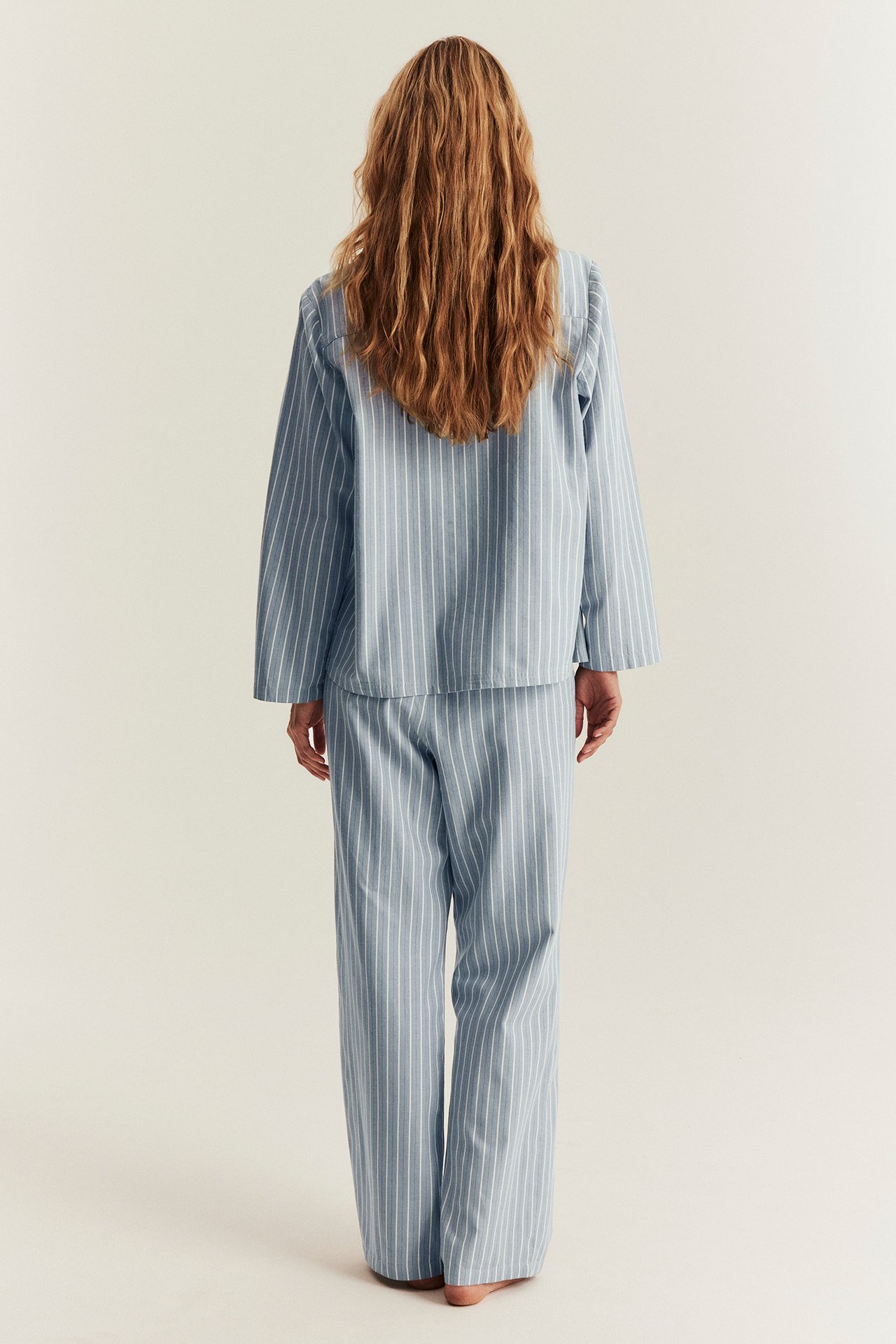 Back view of a woman wearing a loose-fit light blue and white striped cotton pajama set.