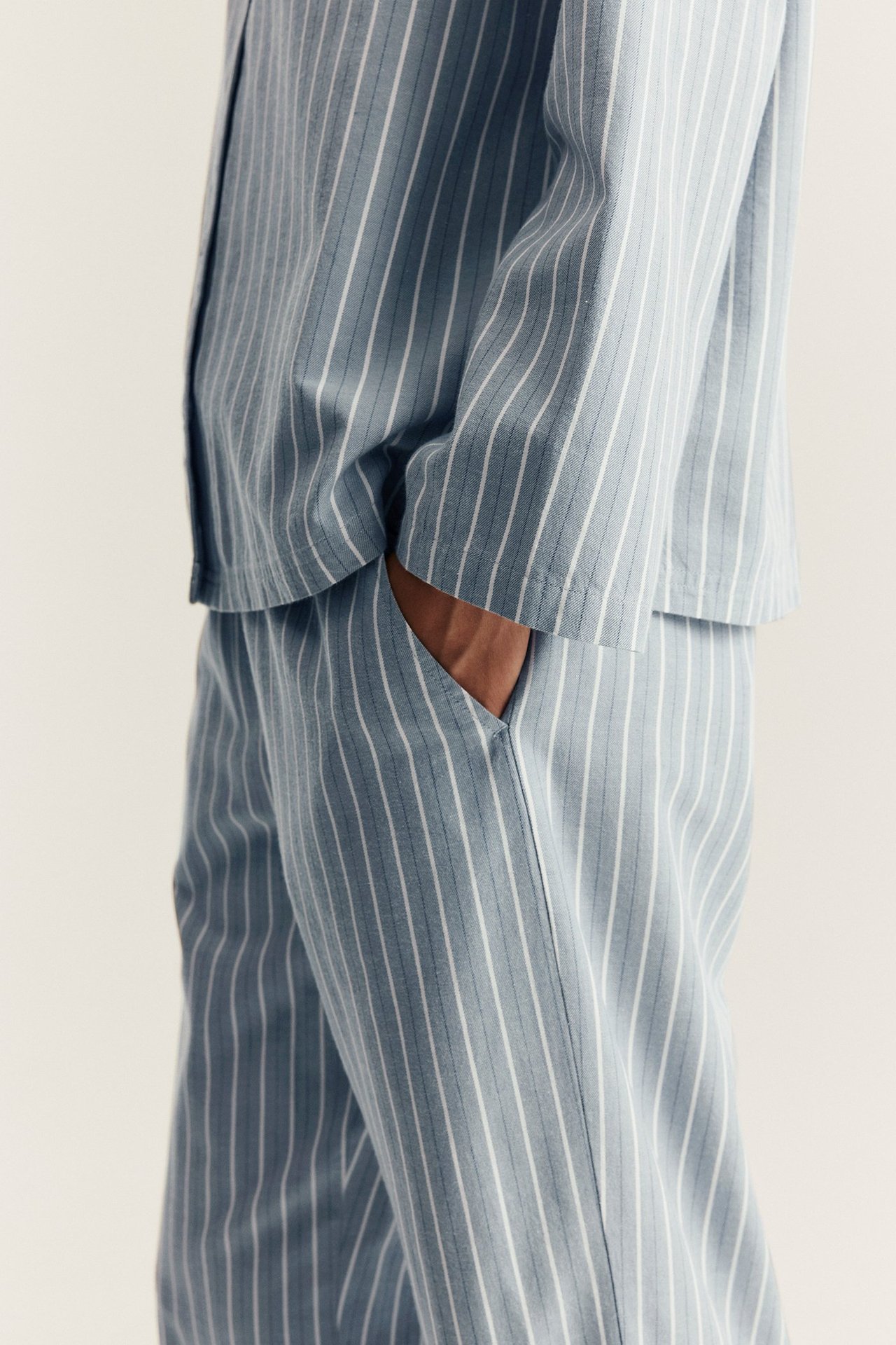Side view: woman in light blue and white striped cotton pajama set, hand in pocket.