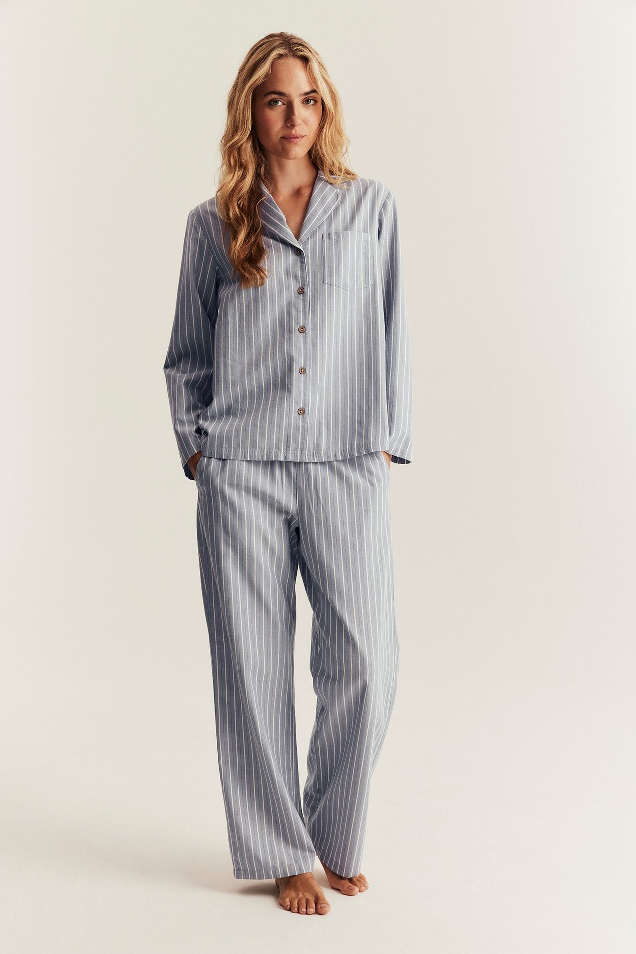 Front view of a woman wearing a light blue striped cotton pyjama set with buttoned shirt and trousers.