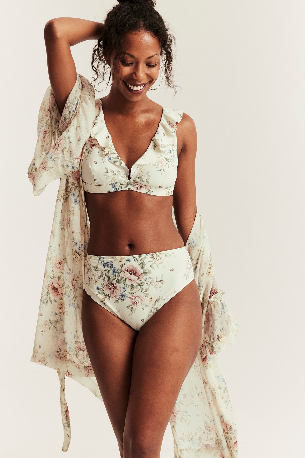 Front view of a woman wearing an off-white floral ruffled bikini top, matching high-waisted bottoms, and sheer kimono.