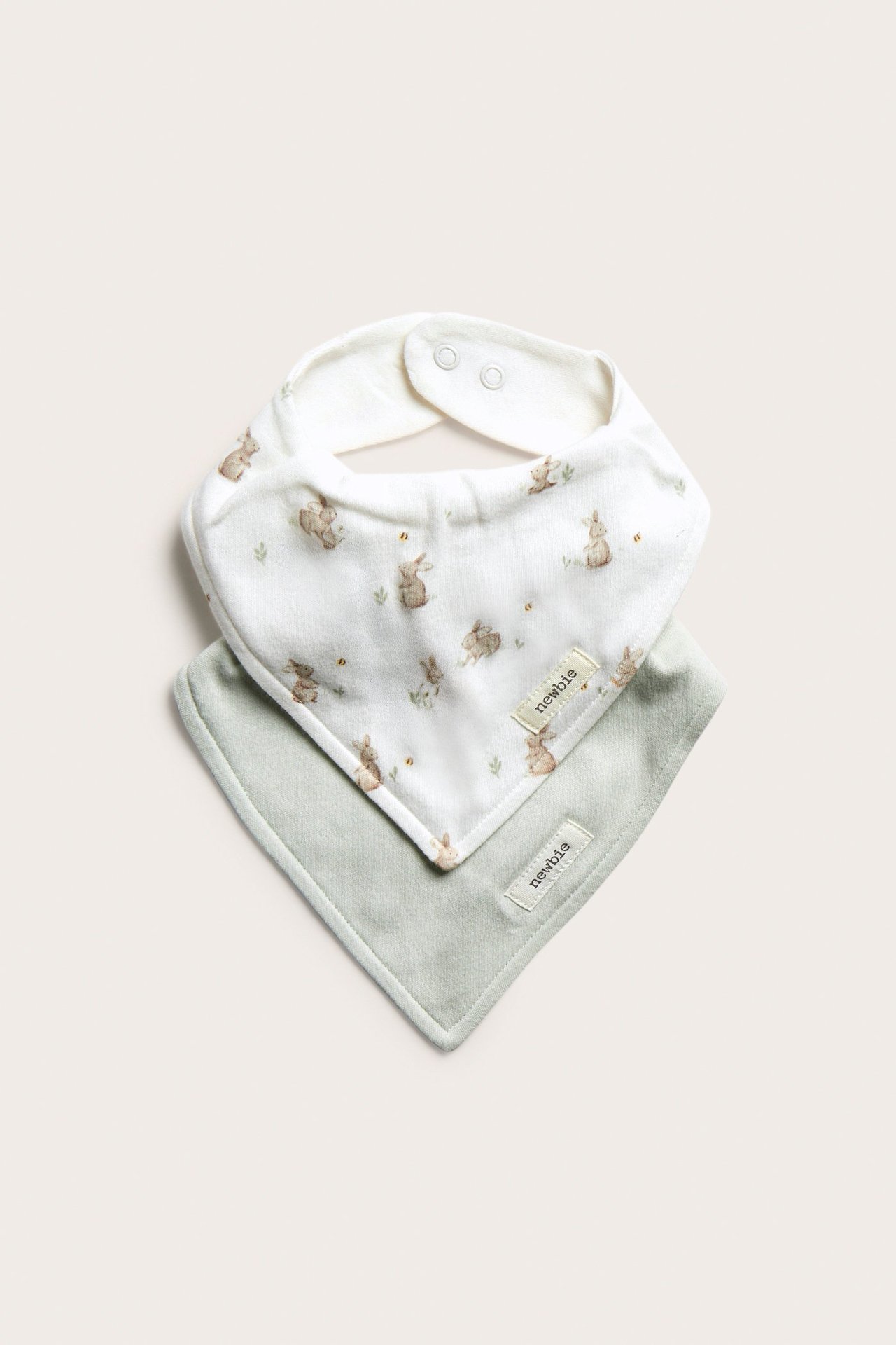 Front view: Two cotton baby bandana bibs, one off-white with rabbit print, one light green, both with snaps.