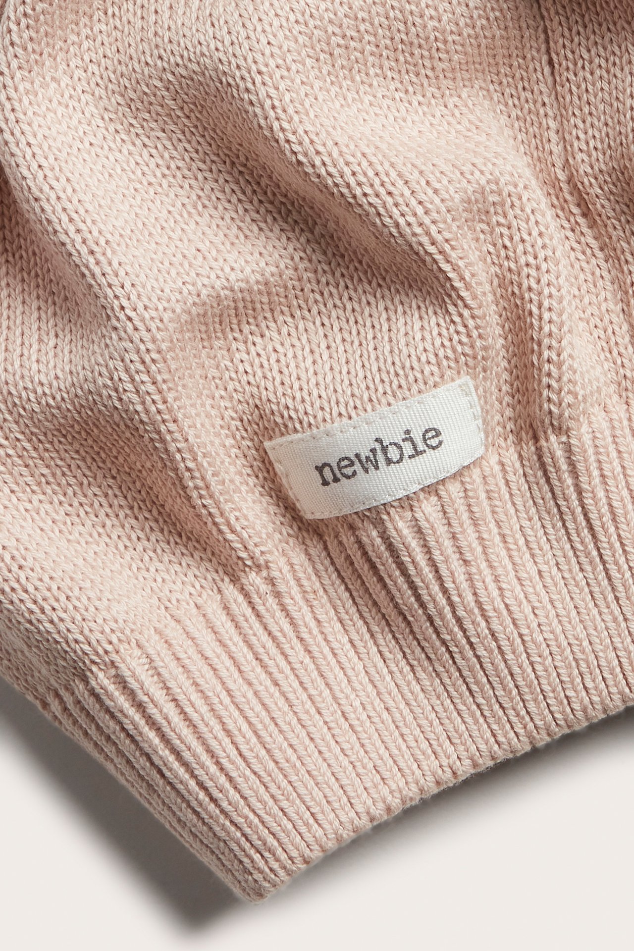 Close-up of light pink knitted fabric with a ribbed edge and a small white label.
