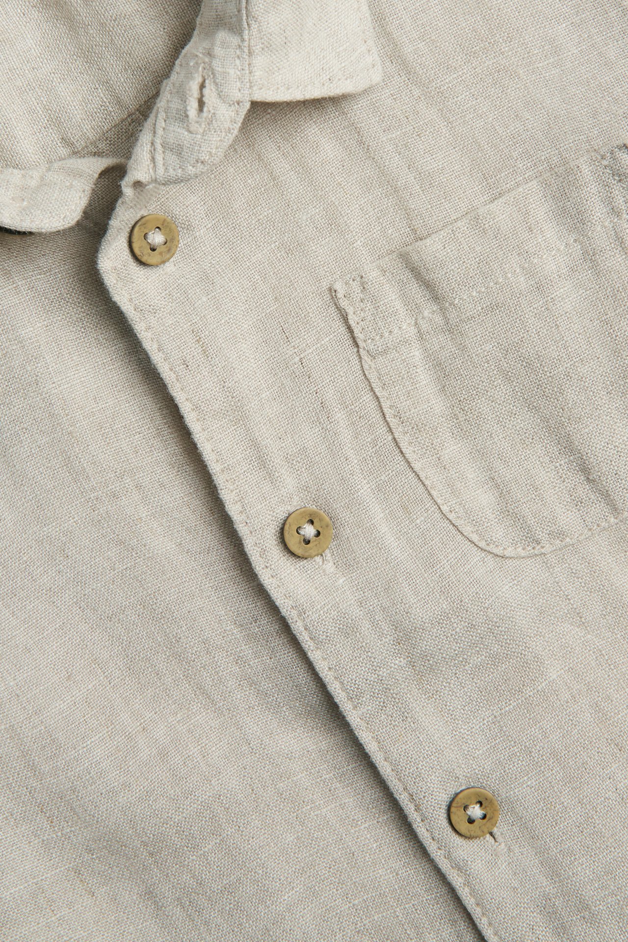 Close-up of a light beige linen shirt with a collar, button placket, and a chest pocket.