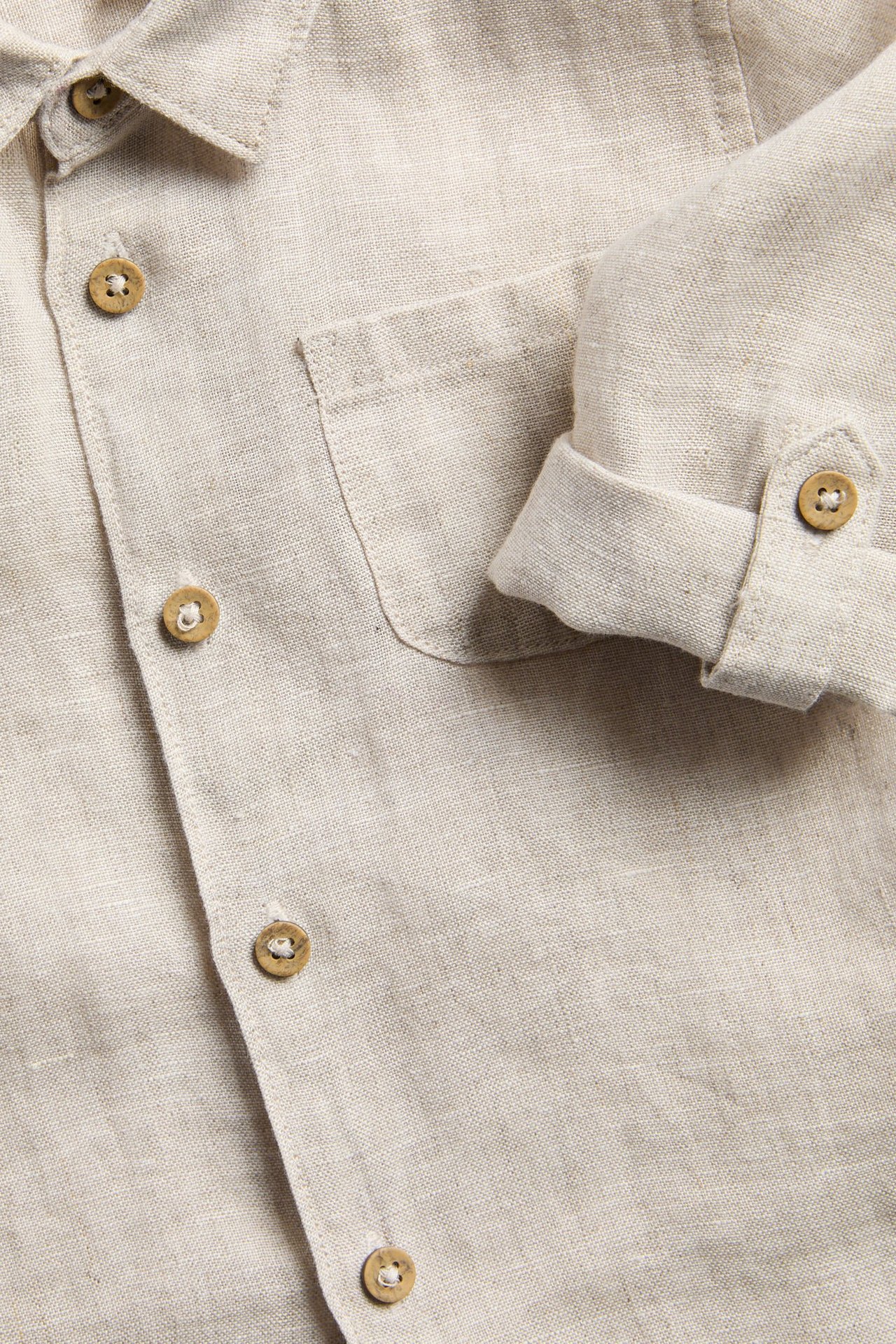 Nahaufnahme eines hellbeigen Leinenhemdes mit Kragen, Knöpfen, Brusttasche und hochgekrempeltem Ärmel.