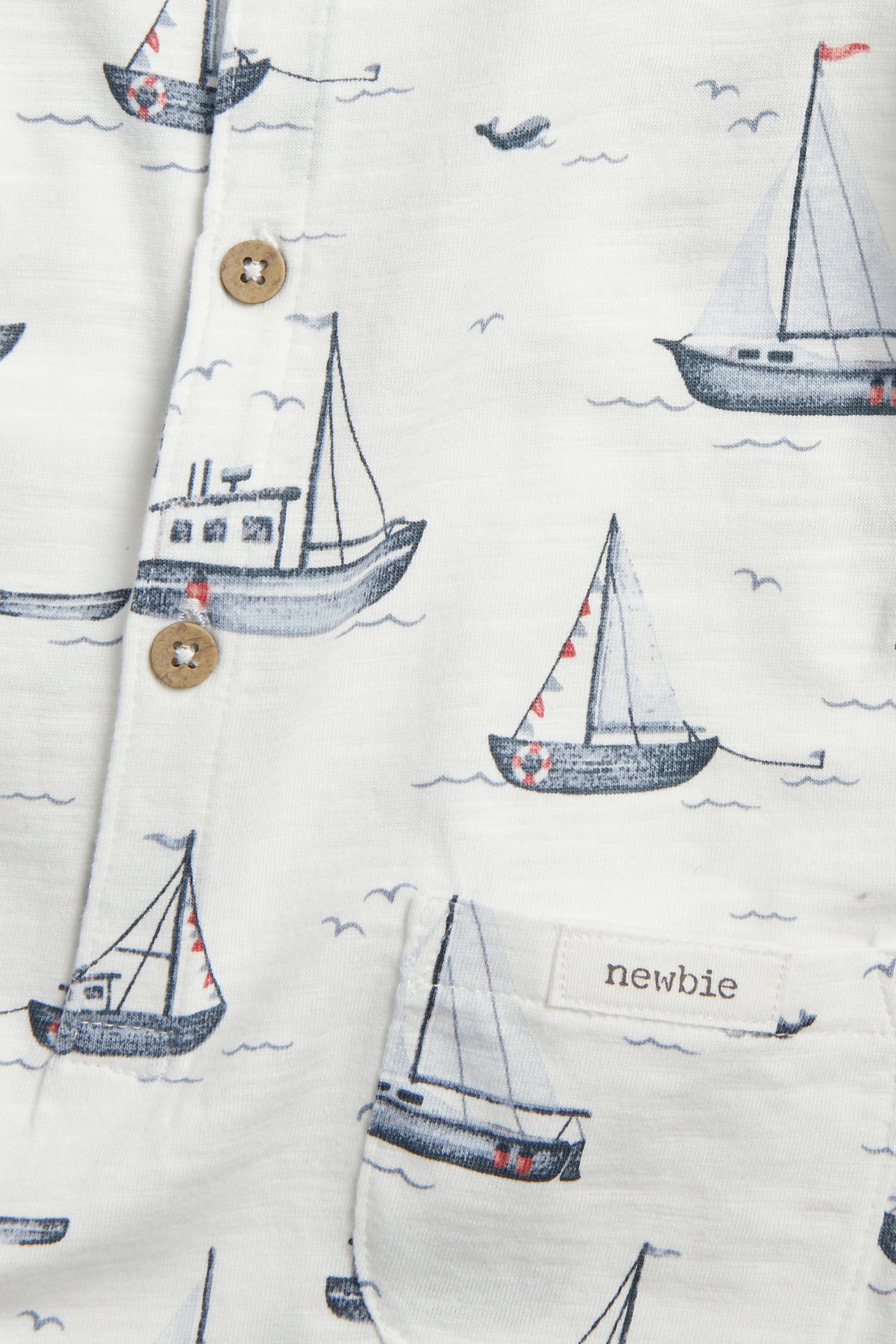Nahaufnahme eines cremeweißen Baumwoll-Slub-Jersey-Stramplers mit Segelbootmuster und Holzknöpfen.