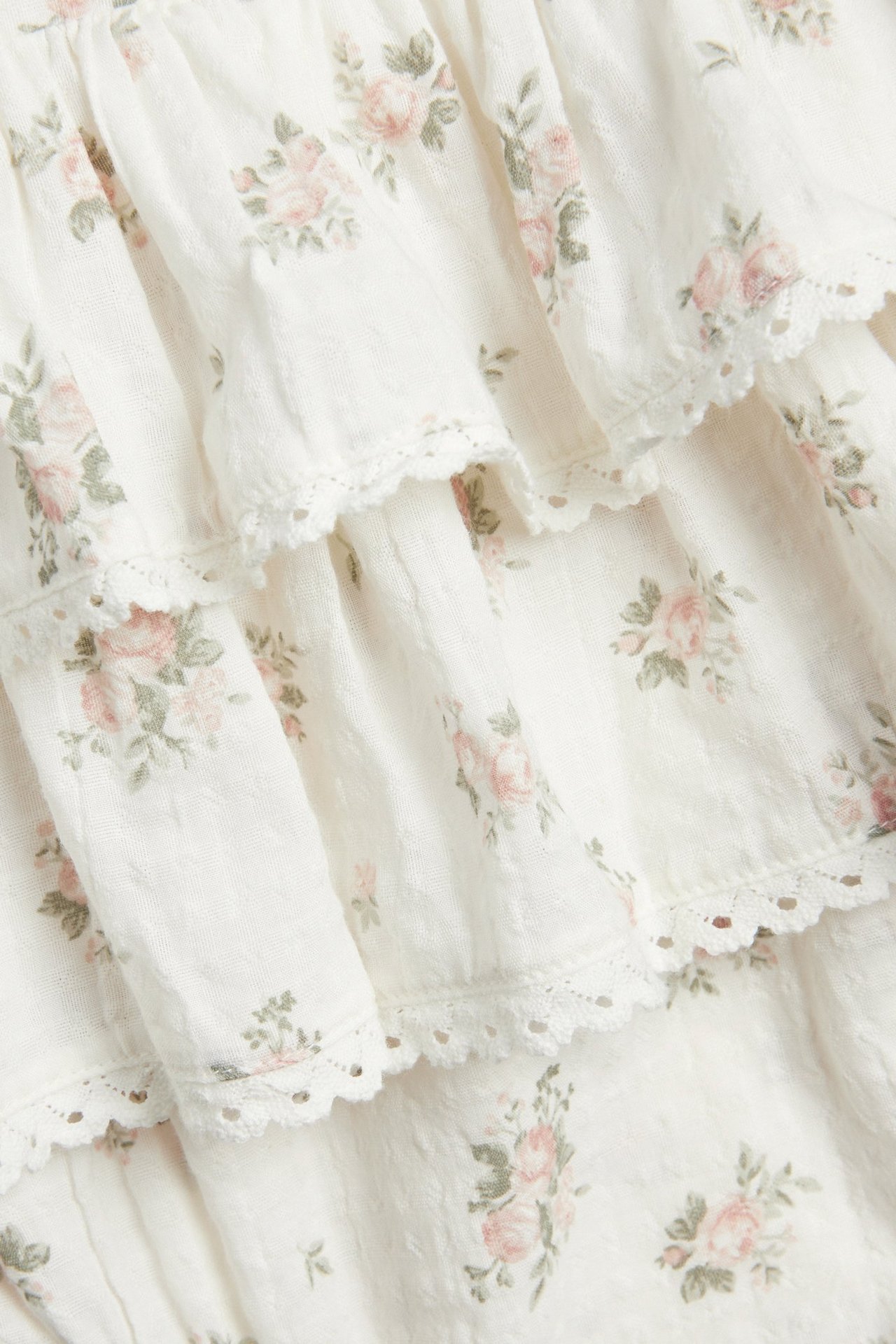 Close-up of an offwhite floral cotton jumpsuit with ruffles and lace trim.
