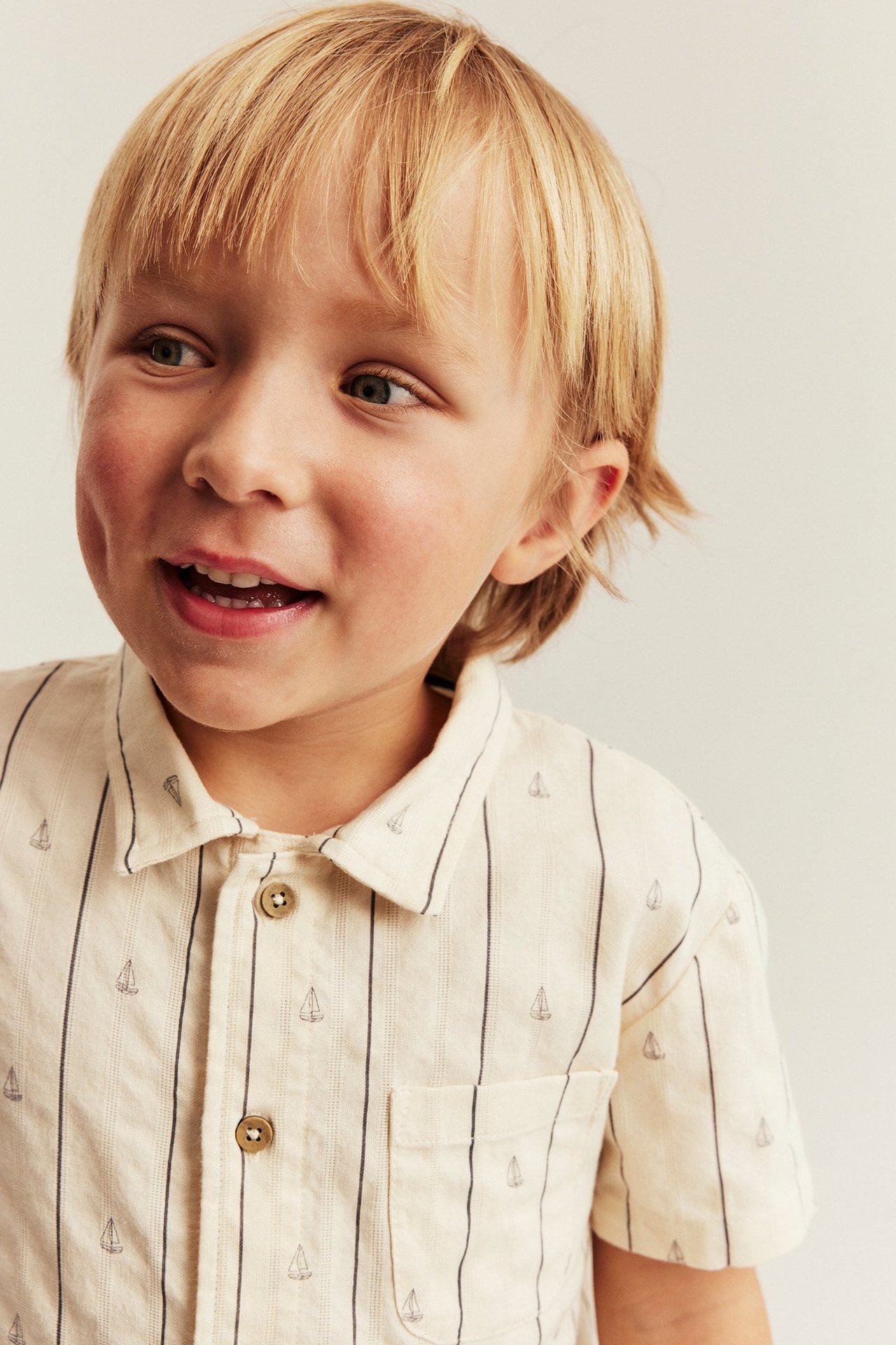 Nahaufnahme Kind in cremefarbenem gestreiften Baumwollhemd mit Segelbootmuster und braunen Knöpfen.