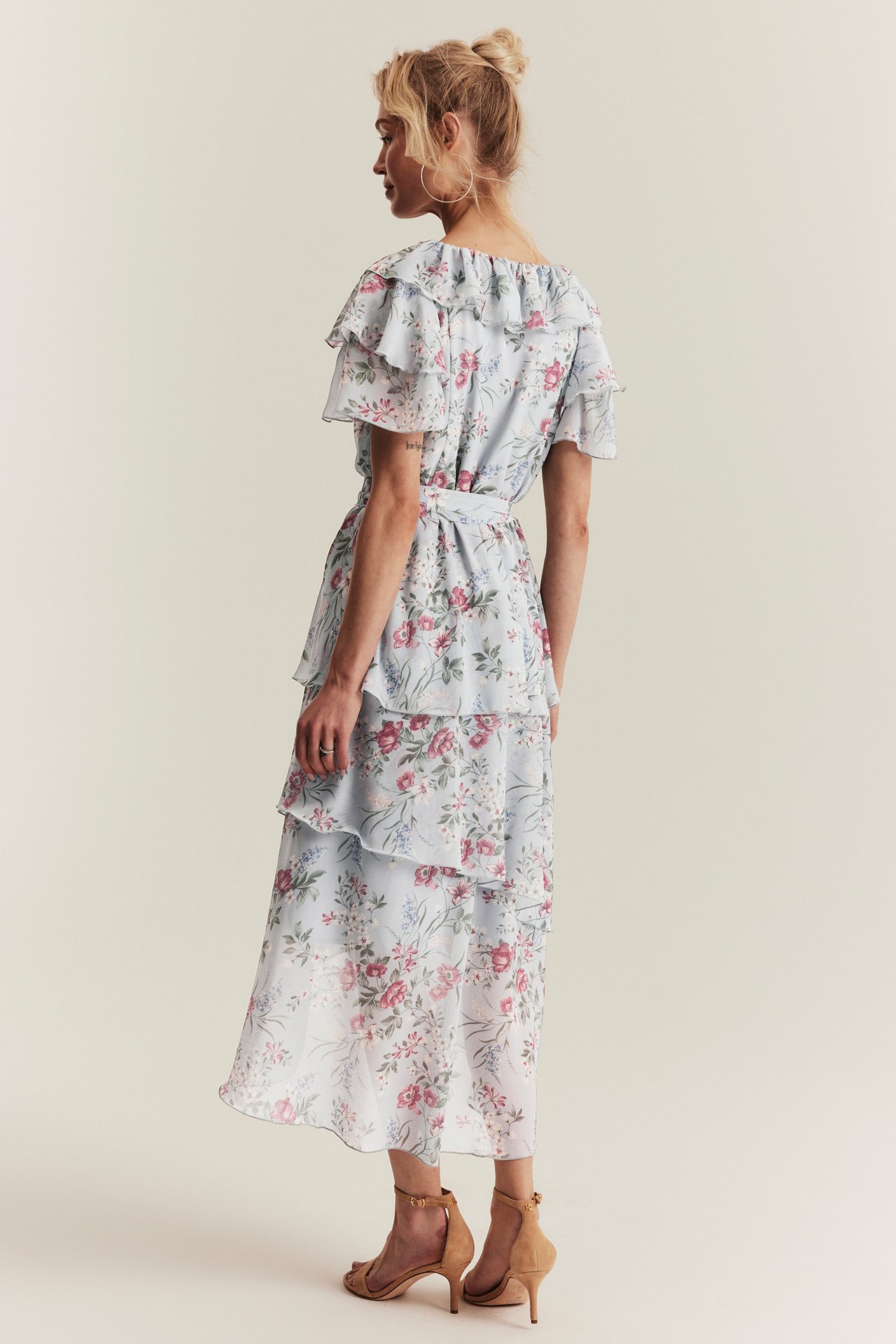 Back view of a woman in a light blue floral tiered ruffle chiffon dress, with light brown heels.